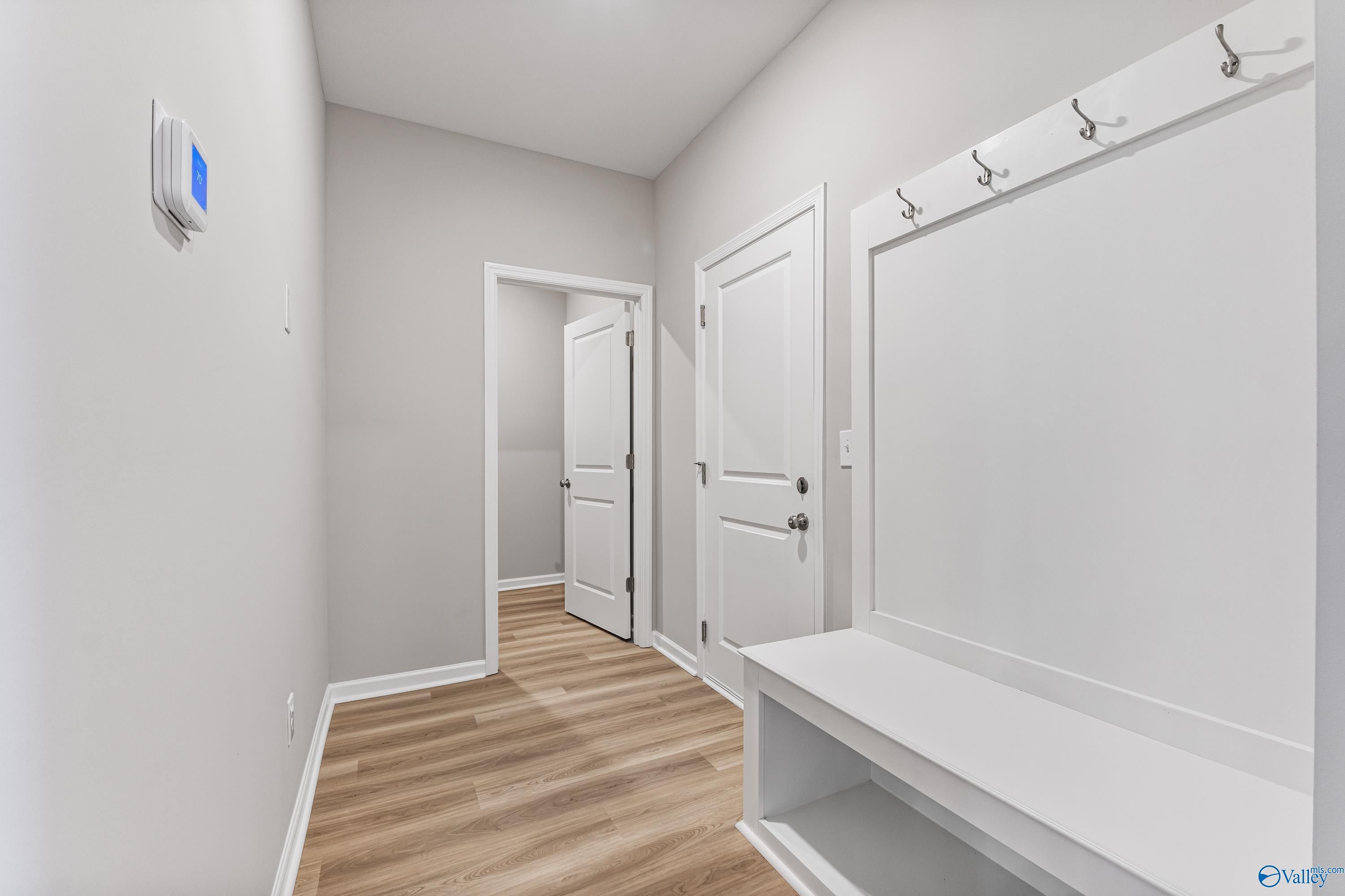 Functional mudroom with built-in bench, coat hooks, and open bedroom doors in Davidson Homes The Phoenix, Hazel Green, Alabama