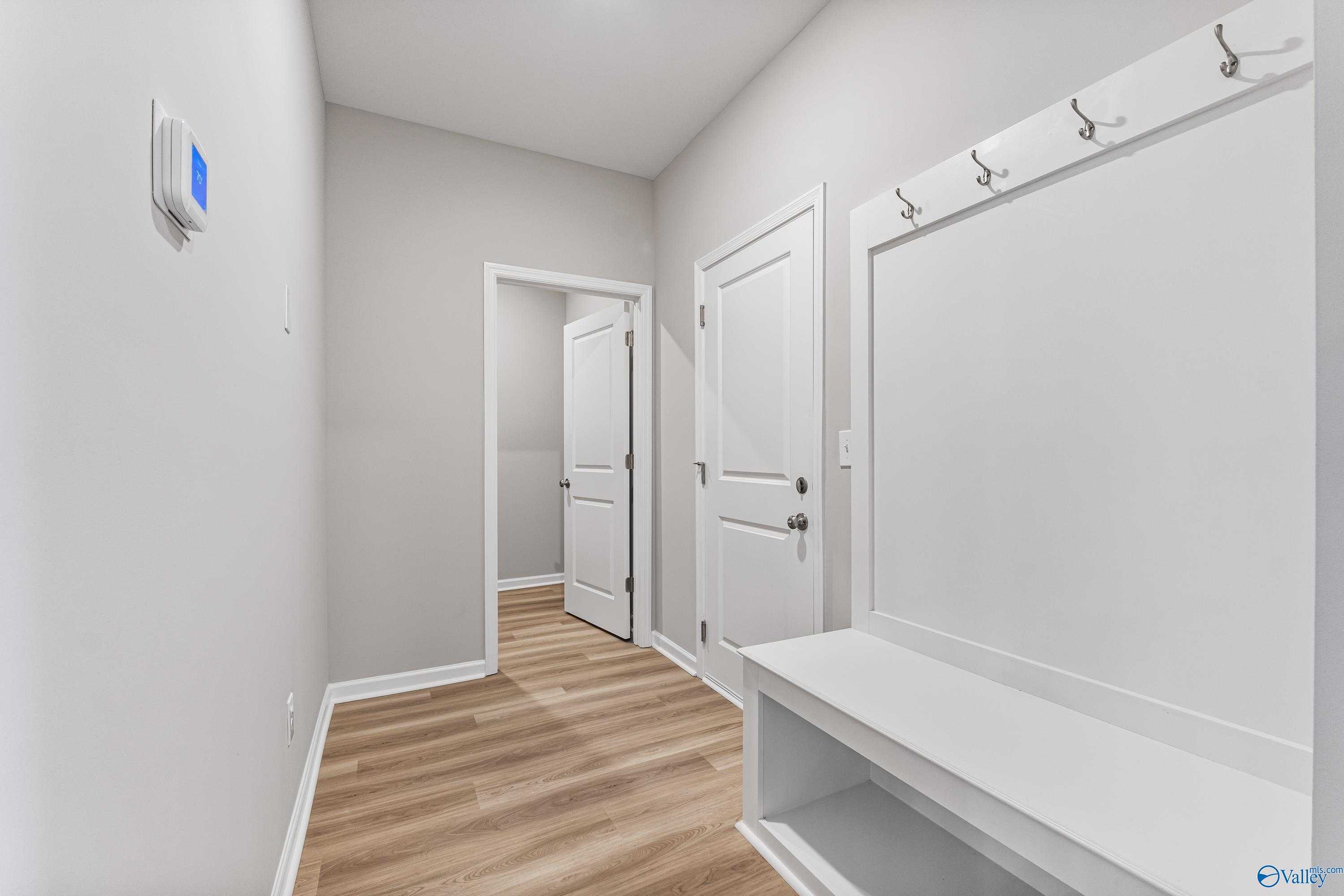 Functional mudroom with built-in bench, coat hooks, and open bedroom doors in Davidson Homes The Phoenix, Hazel Green, Alabama