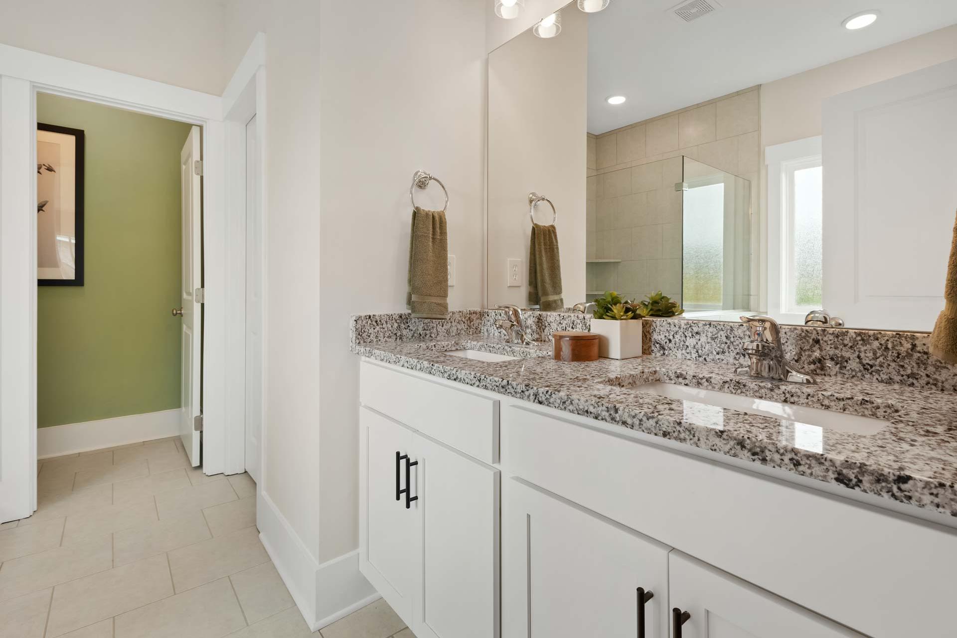 Spacious master bathroom at Durham Farms in Harvest Alabama featuring double granite vanity white cabinets mirrors and glass shower