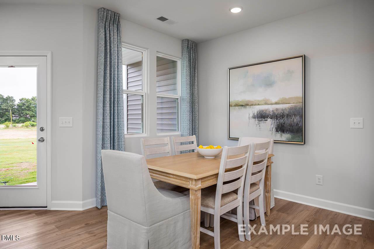 Bright dining room with wooden table, white chairs, fruit bowl, and abstract lake painting in Davidson Homes The Graham, Fuquay-Varina NC