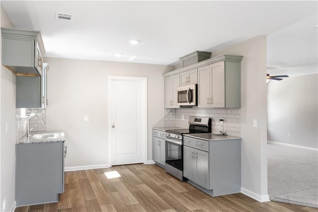 Modern gray shaker cabinet kitchen with stainless steel appliances, white subway tile backsplash, and hardwood floors in Davidson Homes The Washington, Phenix City