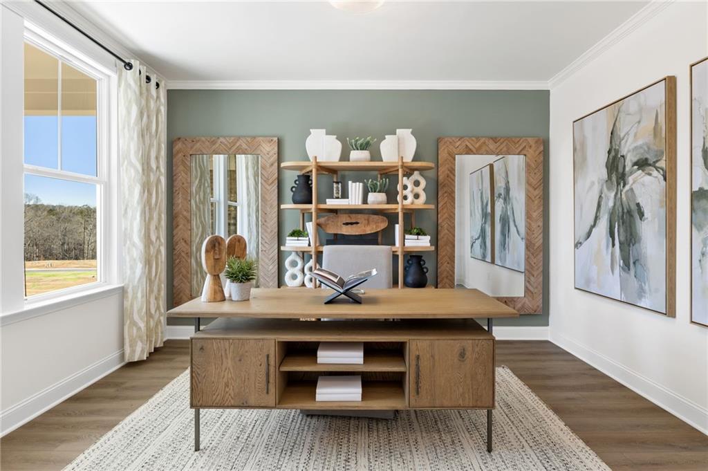 Modern home office with wooden desk, sage green accent wall, abstract art, and window views in Davidson Homes The Aspen A, Buford, GA