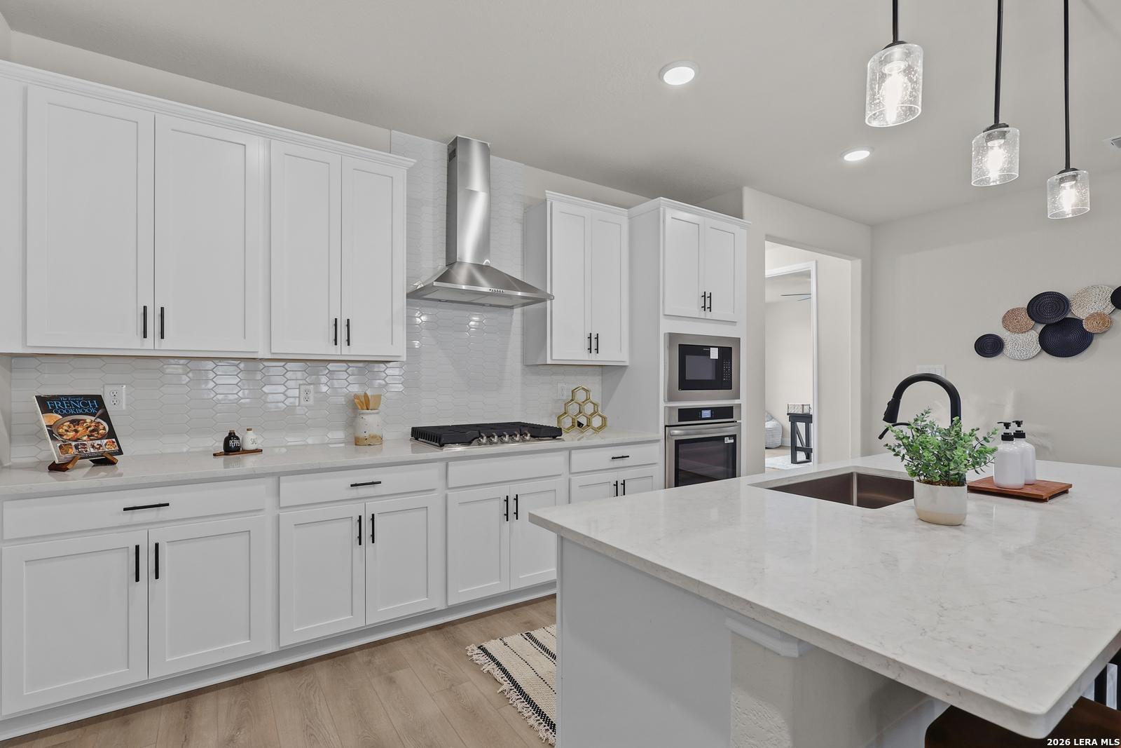 Modern white kitchen with quartz island, stainless steel appliances, hexagon tile backsplash in The Lanier G, Castroville, TX