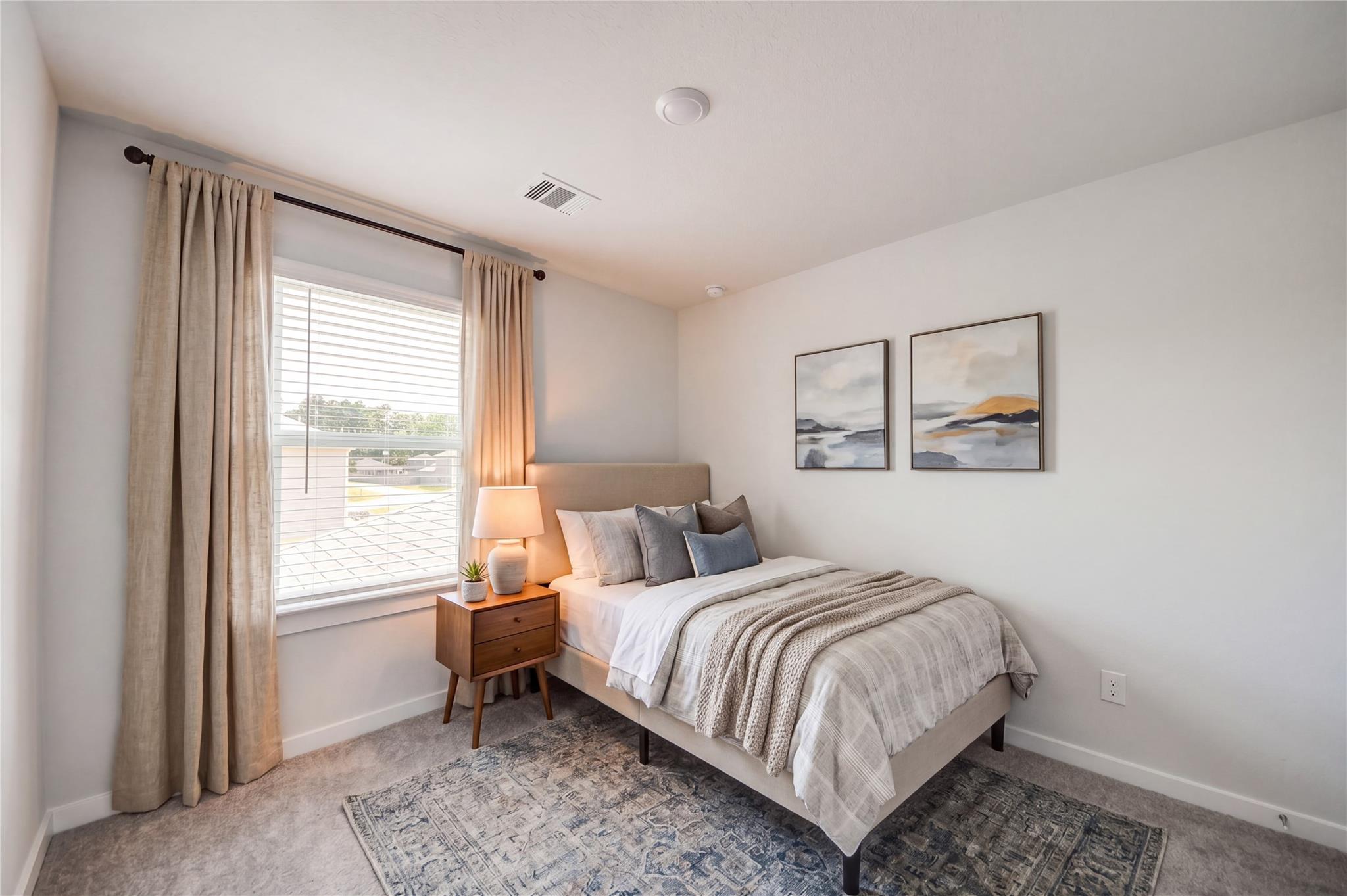 Cozy bedroom with upholstered bed, nightstand, and natural light in The Brazos F floor plan at Liberty Estates, Cleveland, Texas