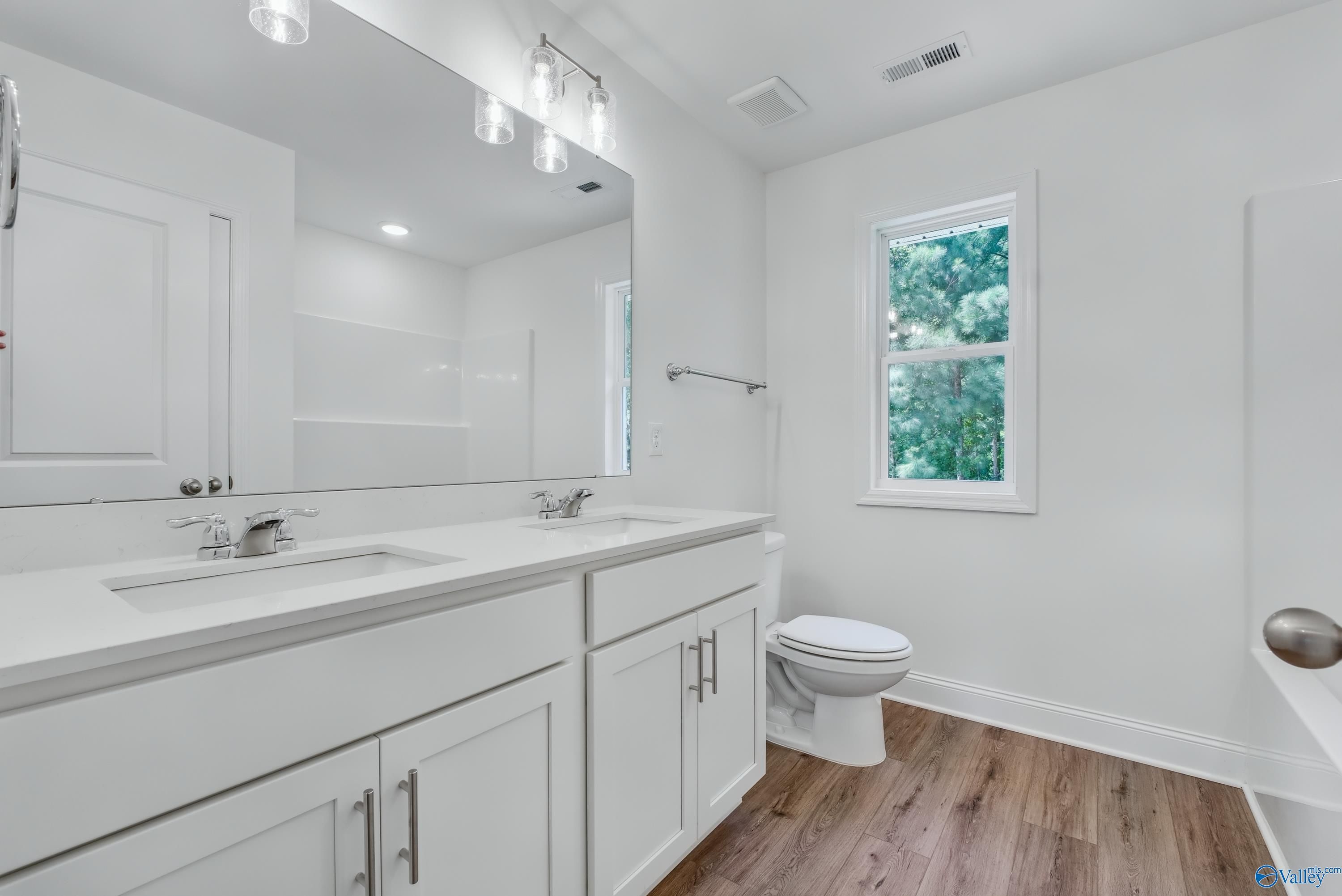 Elegant primary bathroom with double white quartz vanity, lighted mirror, toilet, and garden window in Davidson Homes The Shelby A, Arab AL