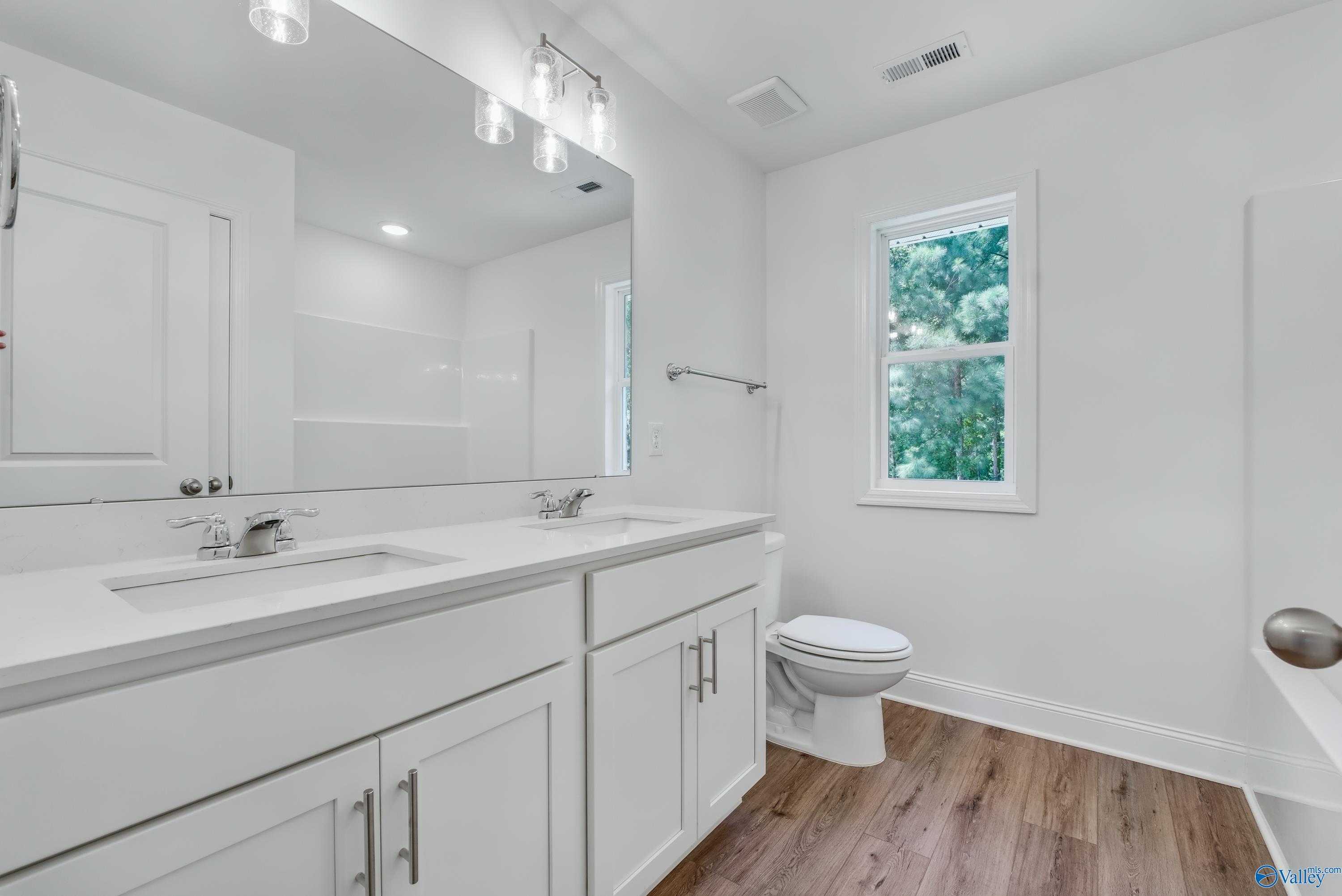 Elegant primary bathroom with double white quartz vanity, lighted mirror, toilet, and garden window in Davidson Homes The Shelby A, Arab AL