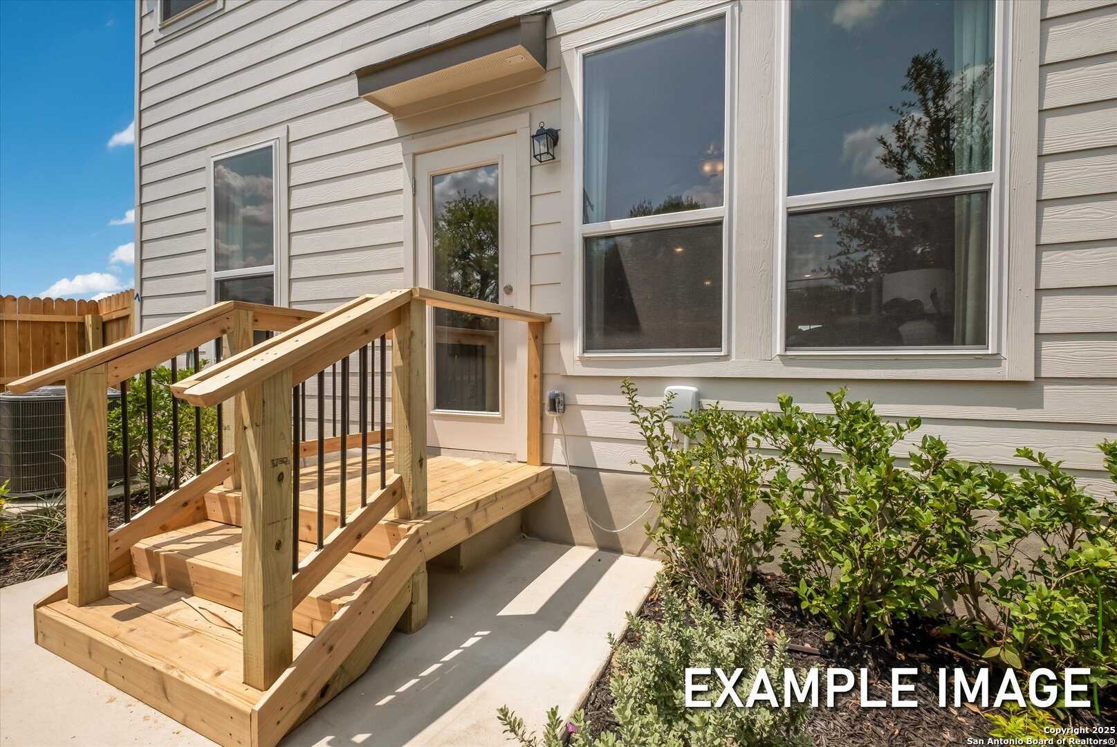 Wooden accessibility ramp with railings to side entrance of beige 4-bedroom The Gillian B home in San Antonio, Texas
