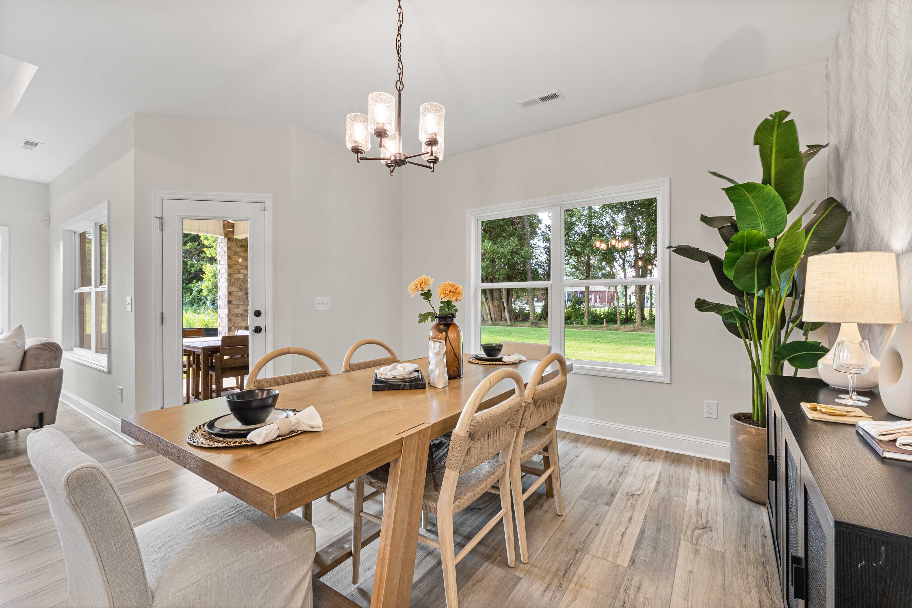 Elegant dining room at Lynn Meadows in Meridianville AL with wooden table, chandelier, large windows, potted plants, and hardwood floors