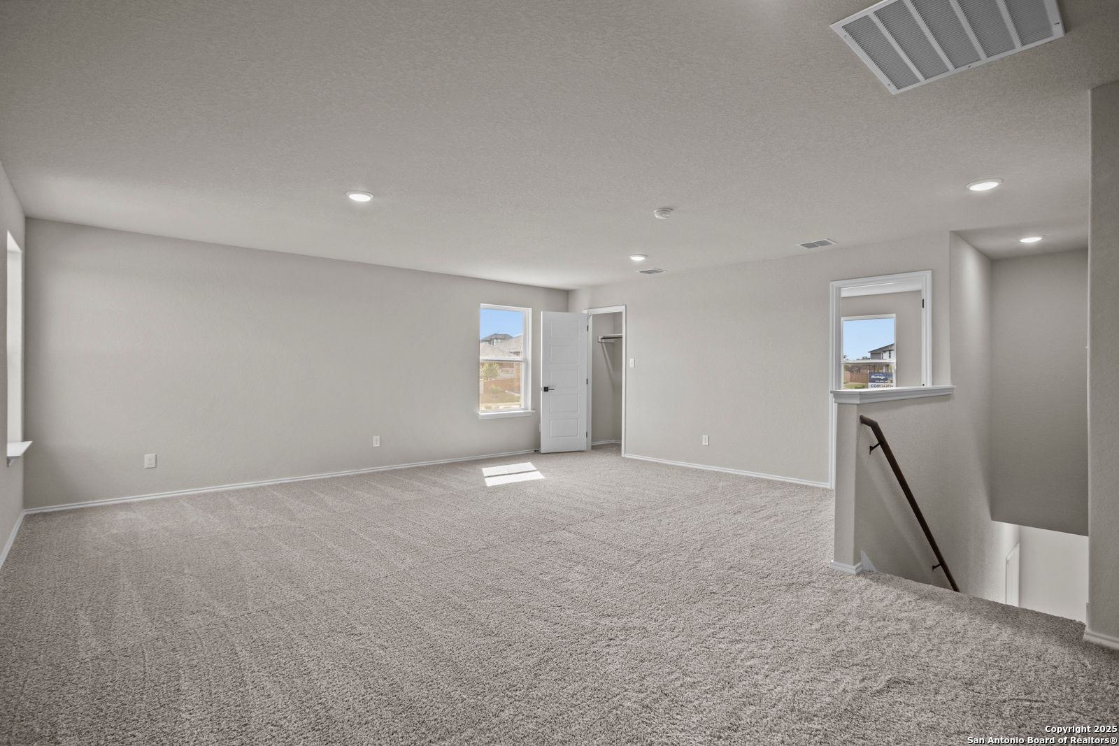 Spacious upstairs loft with beige carpet, large windows, recessed lights, and staircase in Davidson Homes The Douglas F, San Antonio