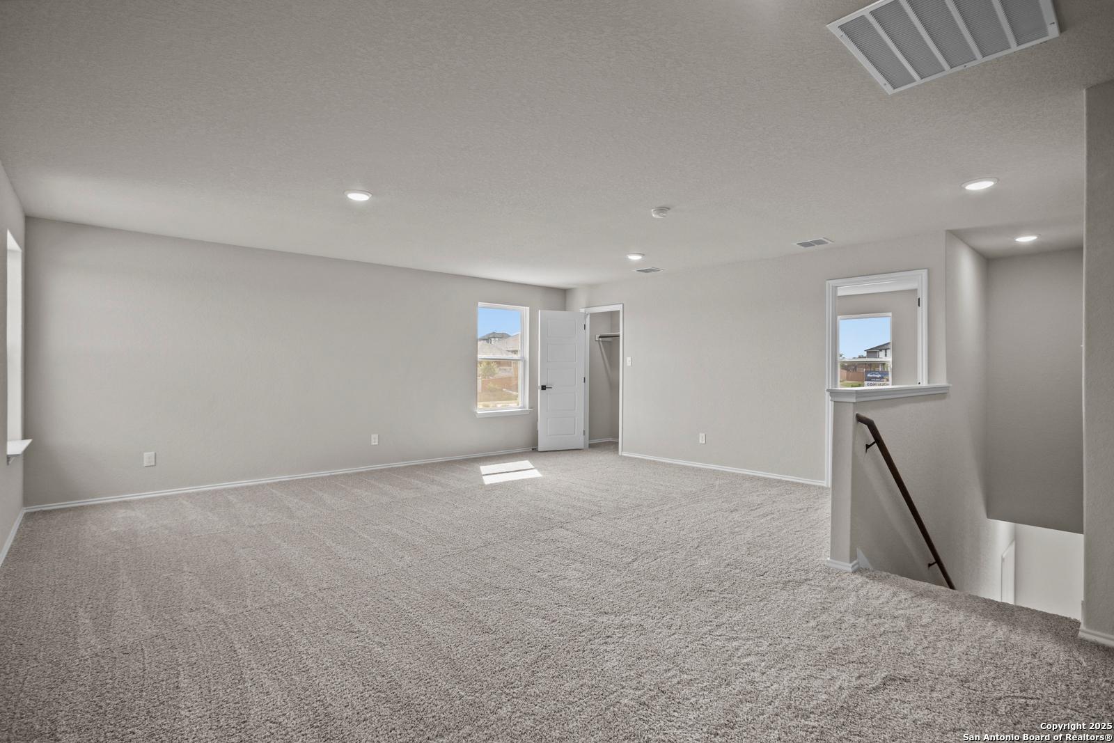 Spacious upstairs loft with beige carpet, large windows, recessed lights, and staircase in Davidson Homes The Douglas F, San Antonio