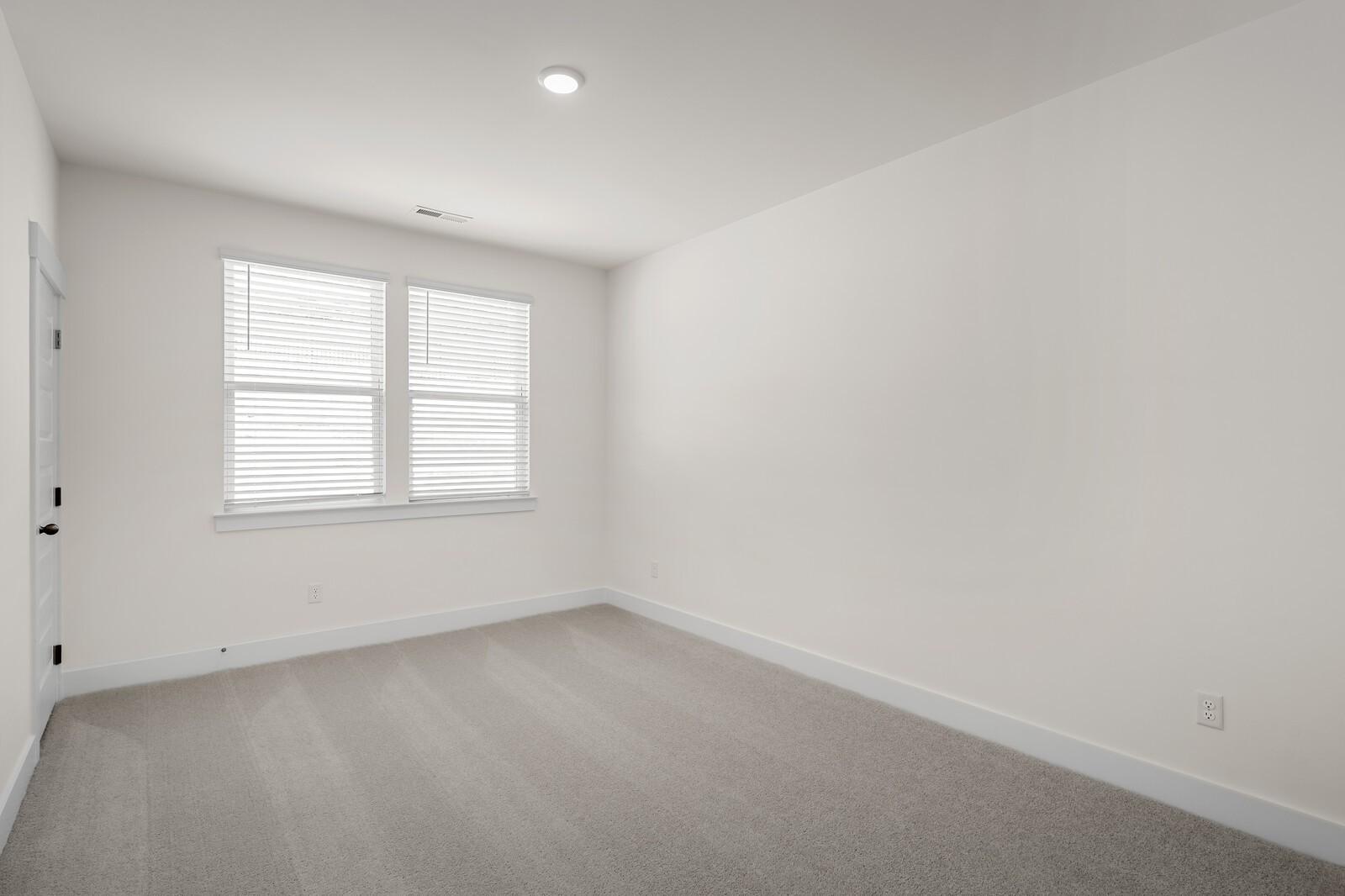 Bright, carpeted bedroom with neutral walls in The Willow floor plan at Woods Crossing in Gallatin, Tennessee.