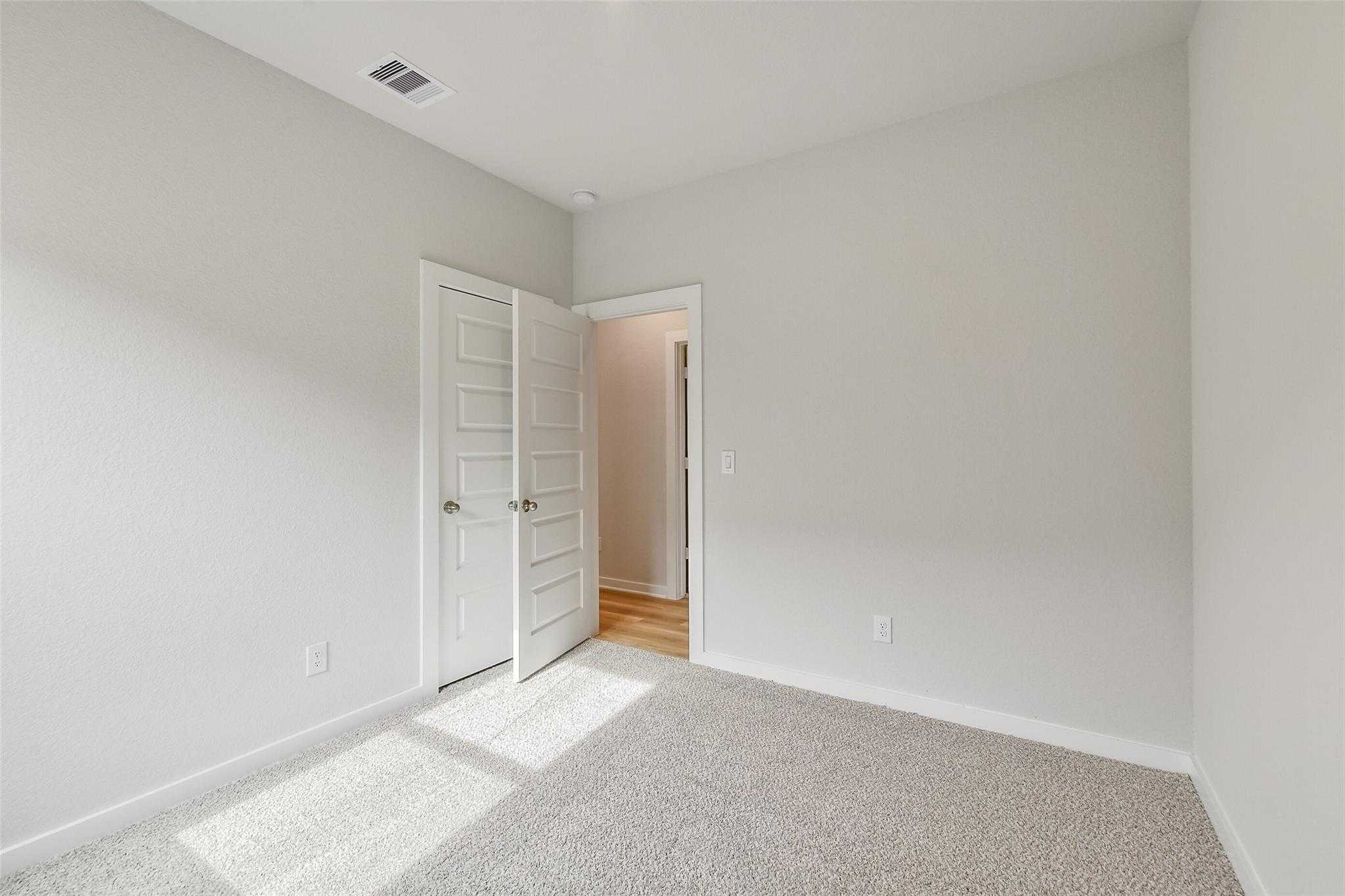 Bright secondary bedroom with light gray walls, white doors, and plush carpet in Davidson Homes The Colorado G, Magnolia, Texas