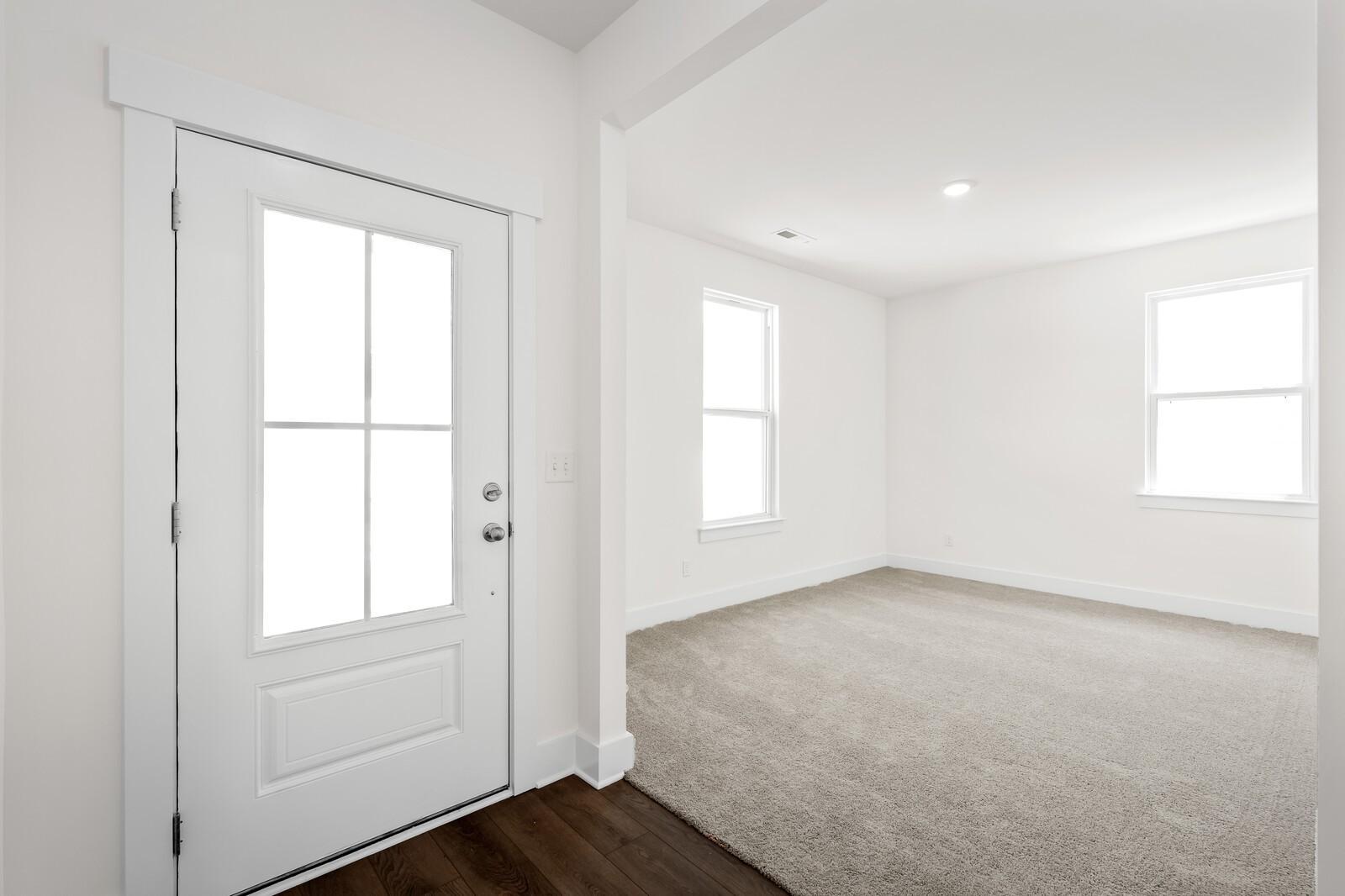 Bright entryway with glass-paneled white front door and carpeted living room in Davidson Homes Cottonwood E, Gallatin, Tennessee
