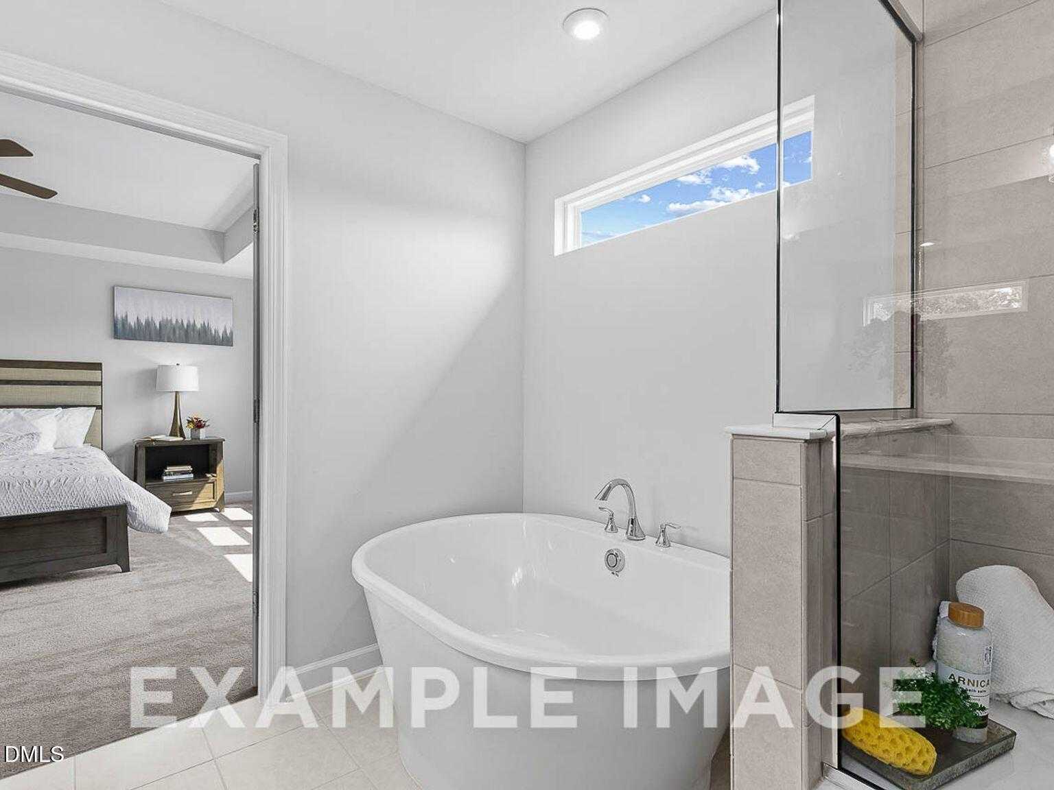 Elegant master bathroom with freestanding tub, glass shower, and bedroom view in Davidson Homes The Chestnut B, Lillington, NC