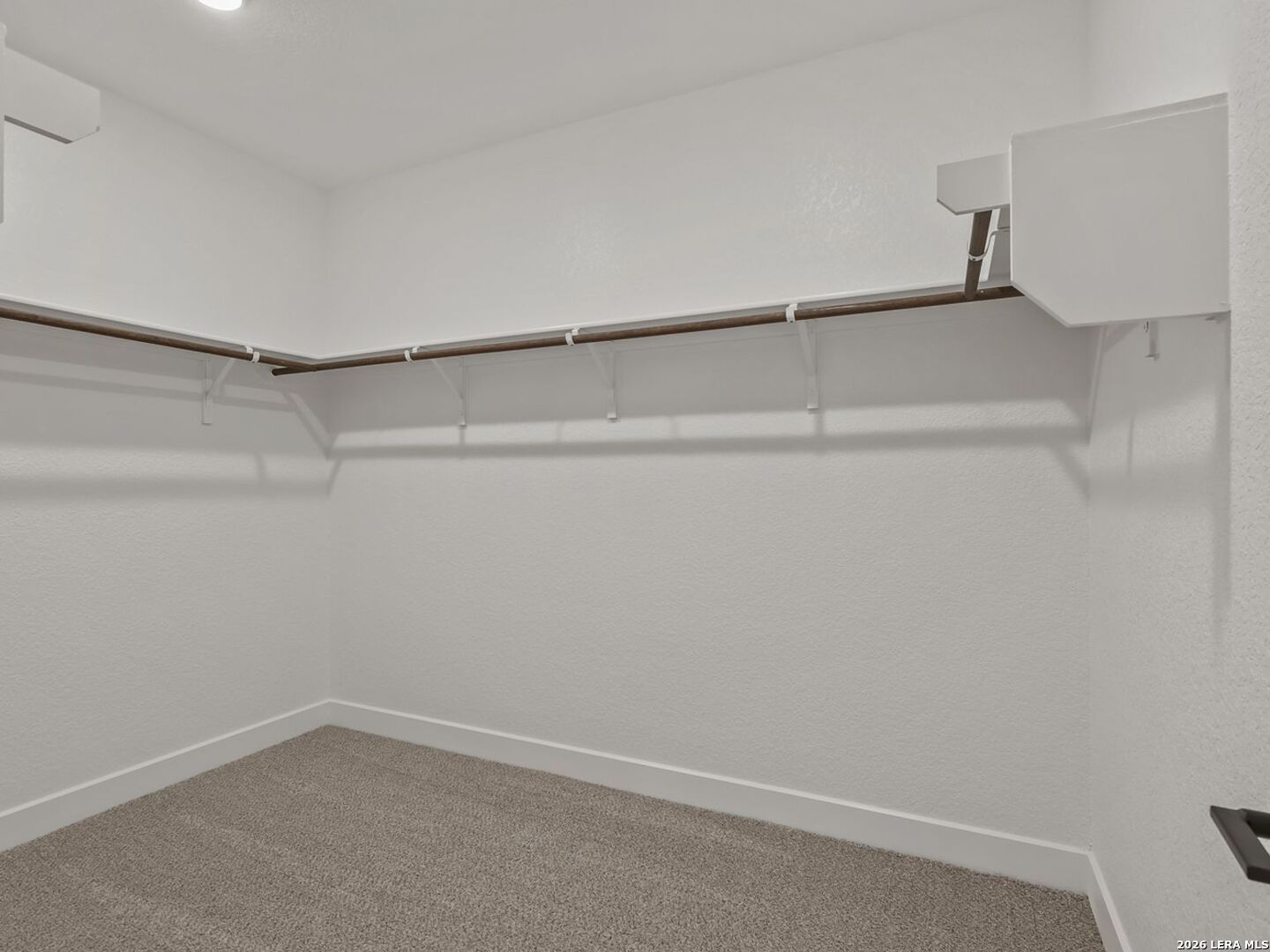 Walk-in closet with carpeted flooring and shelving in The Belmont H floor plan at Potranco Oaks in Castroville, Texas.