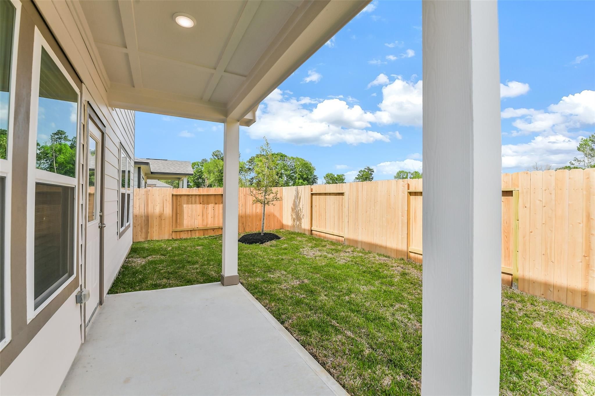 Covered patio with white columns and concrete slab overlooking fenced grassy backyard in Davidson Homes San Marcos E, Conroe Texas