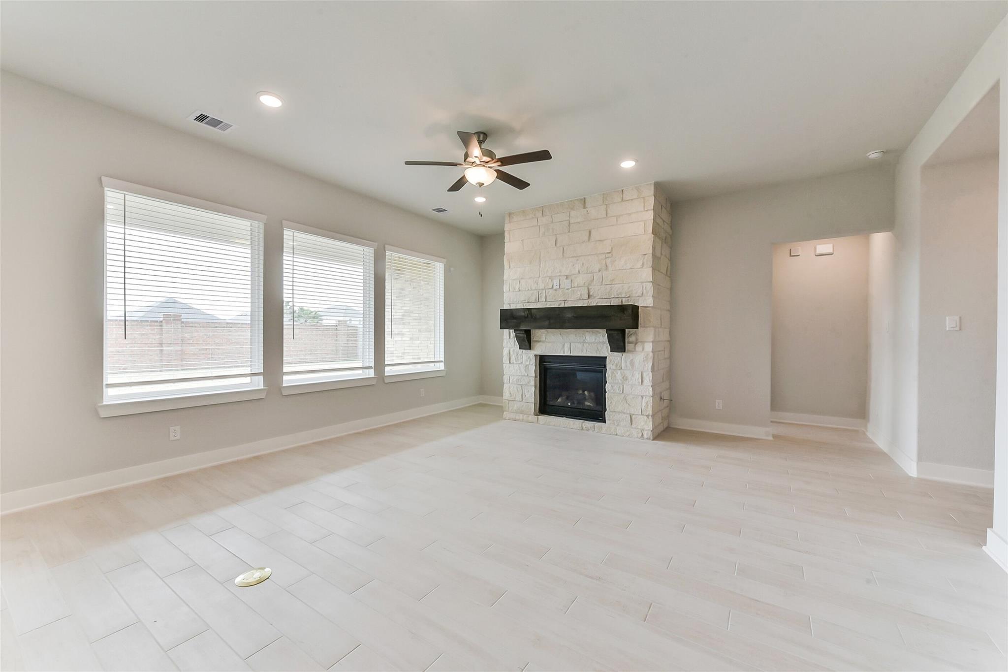 Spacious living room with stone fireplace, ceiling fan, and large windows in Davidson Homes The Edward C, Lago Mar, Texas City