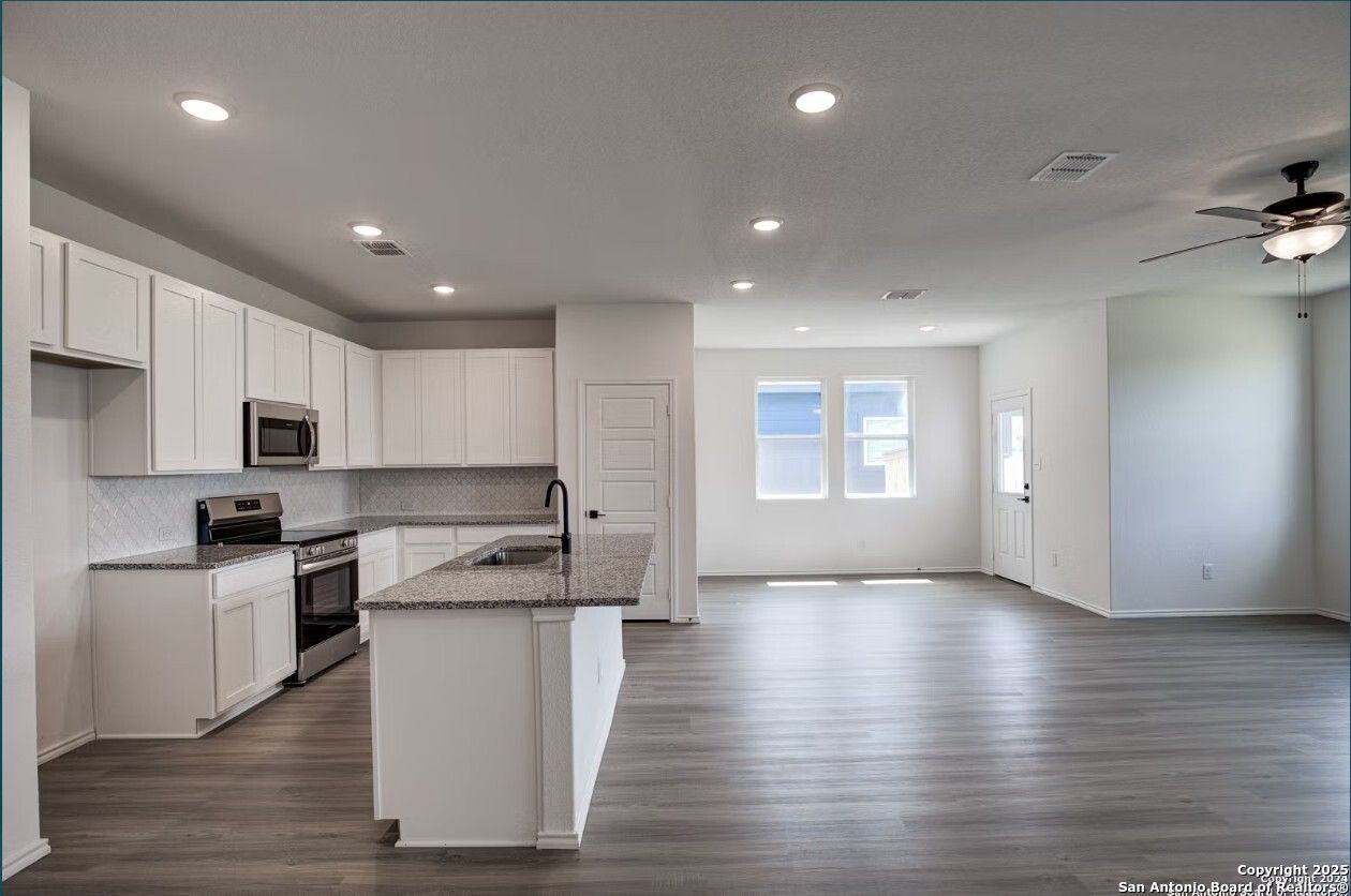 Modern open-concept kitchen with white cabinets, granite island, stainless appliances in Davidson Homes The Daphne H, Seguin, Texas