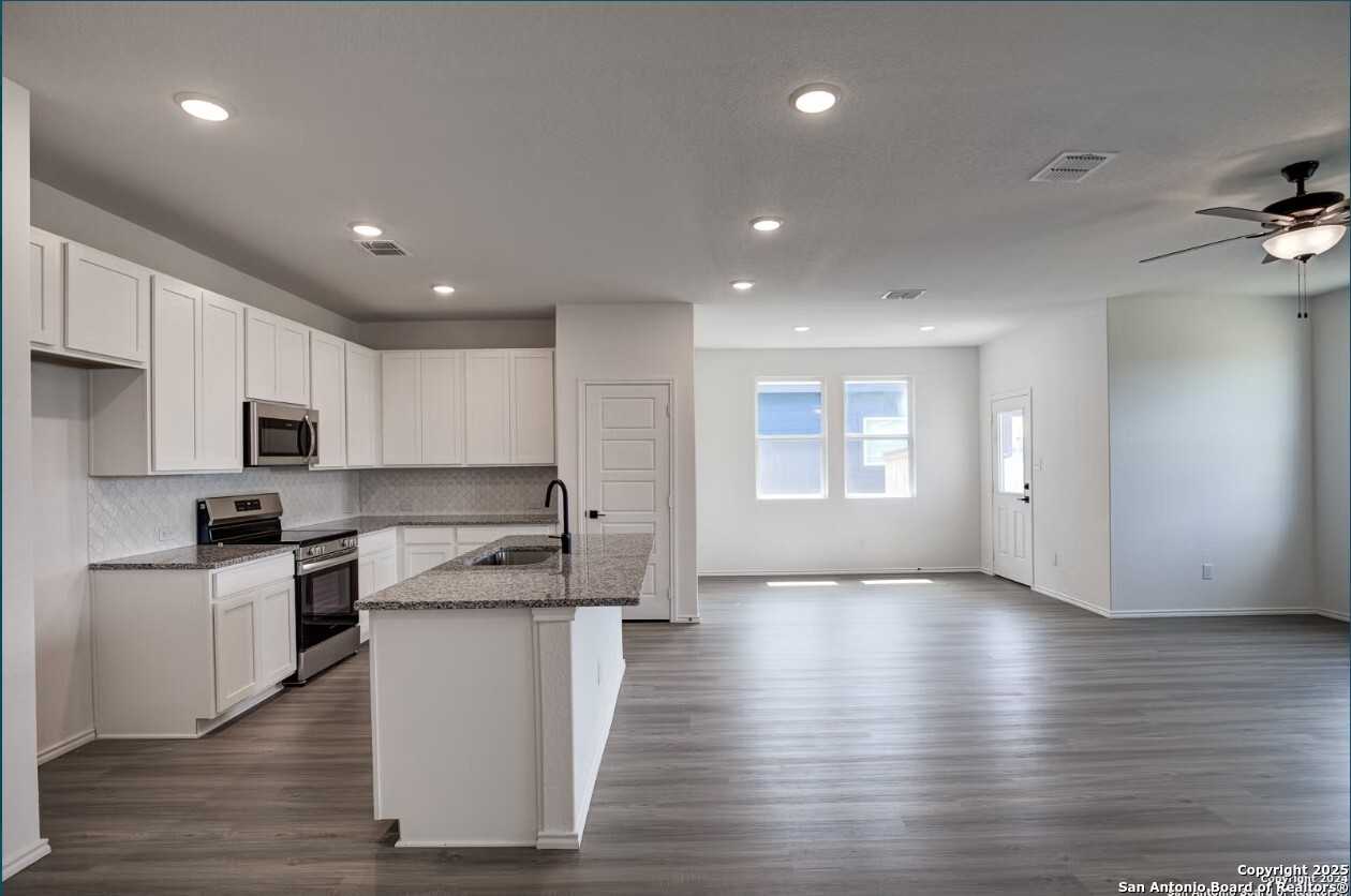 Modern open-concept kitchen with white cabinets, granite island, stainless appliances in Davidson Homes The Daphne H, Seguin, Texas