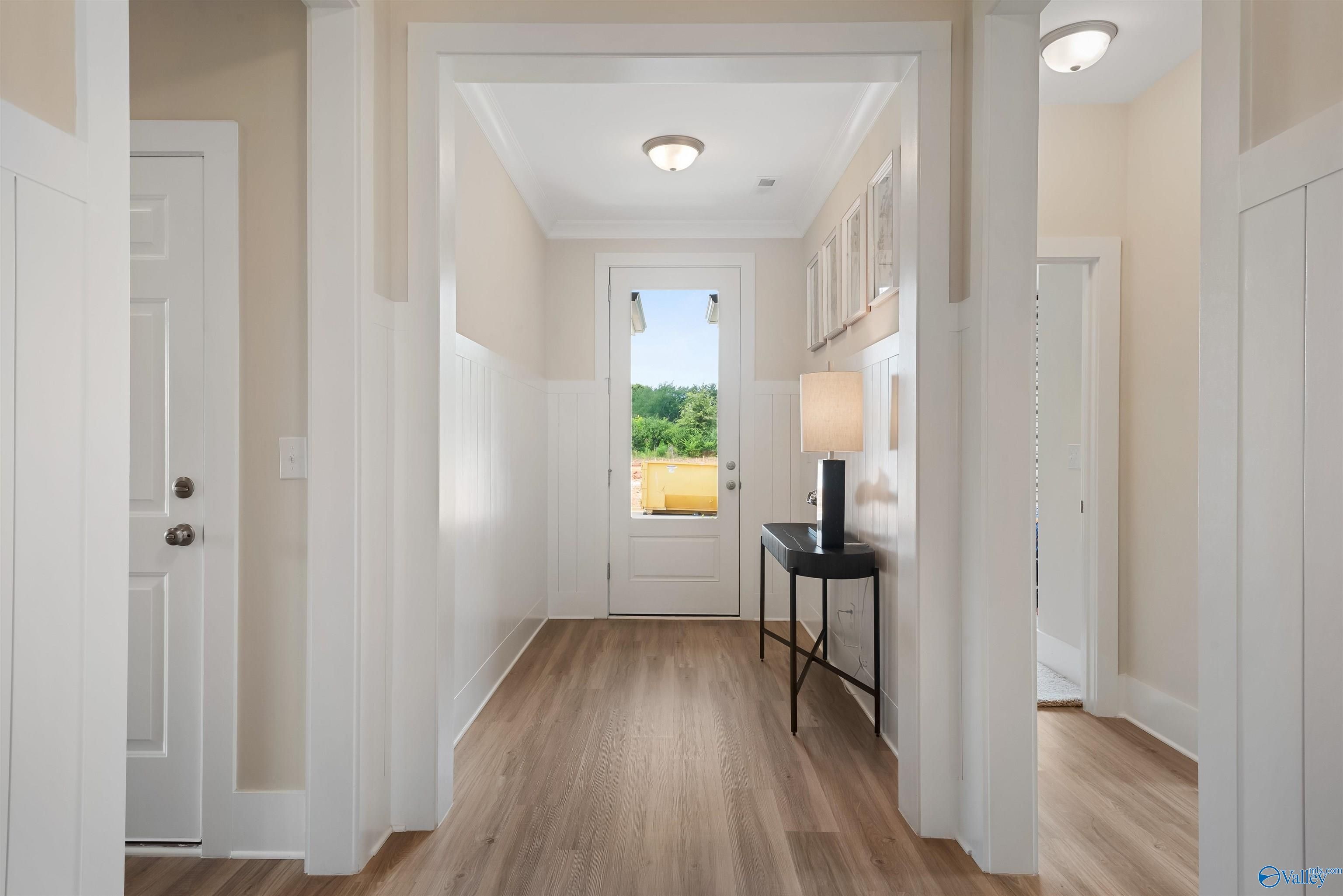Bright entry foyer with light wood floors, arched openings, console table, lamp, and green field view through glass door in Davidson Homes The Everett, New Market, Alabama