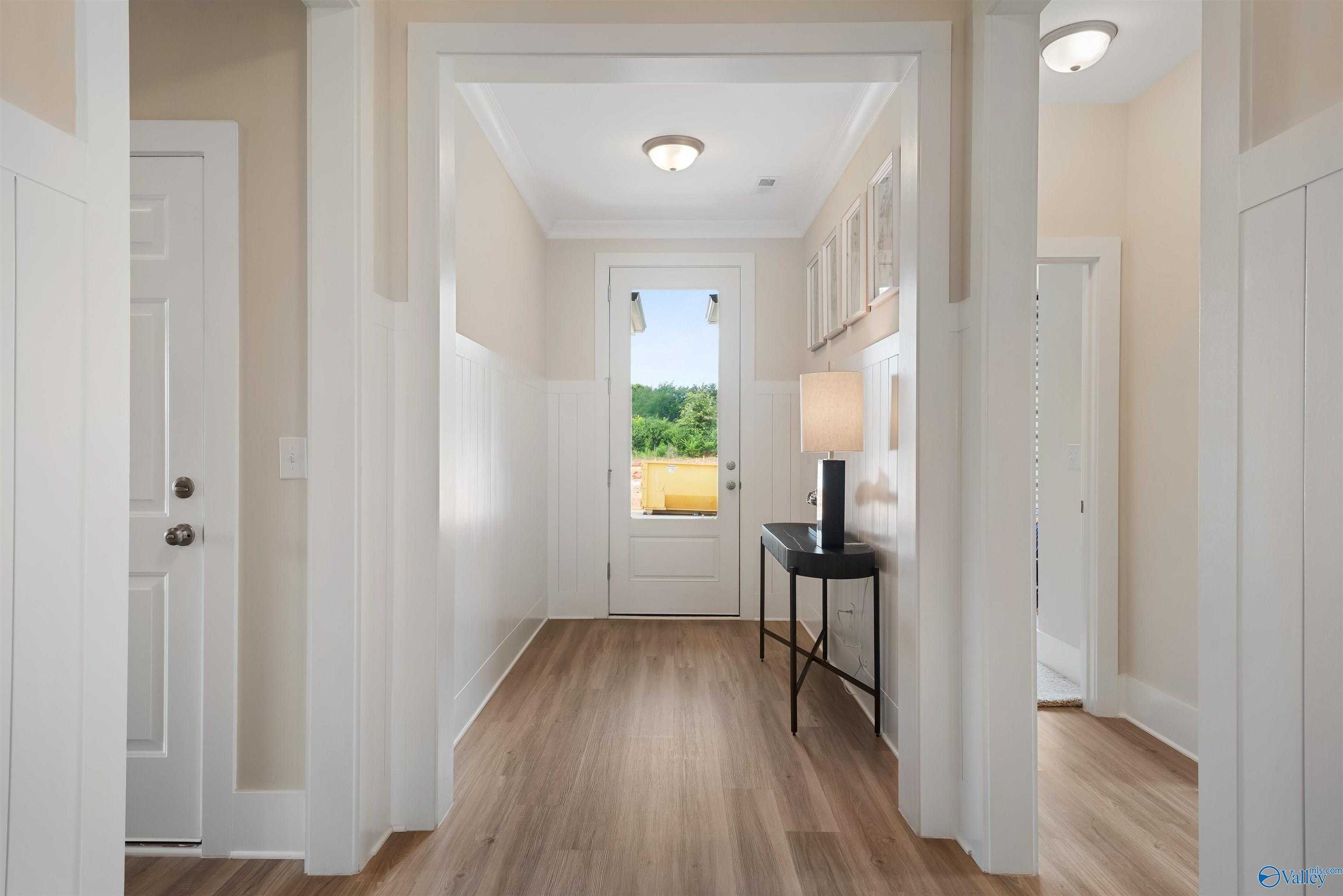 Bright entry foyer with light wood floors, arched openings, console table, lamp, and green field view through glass door in Davidson Homes The Everett, New Market, Alabama