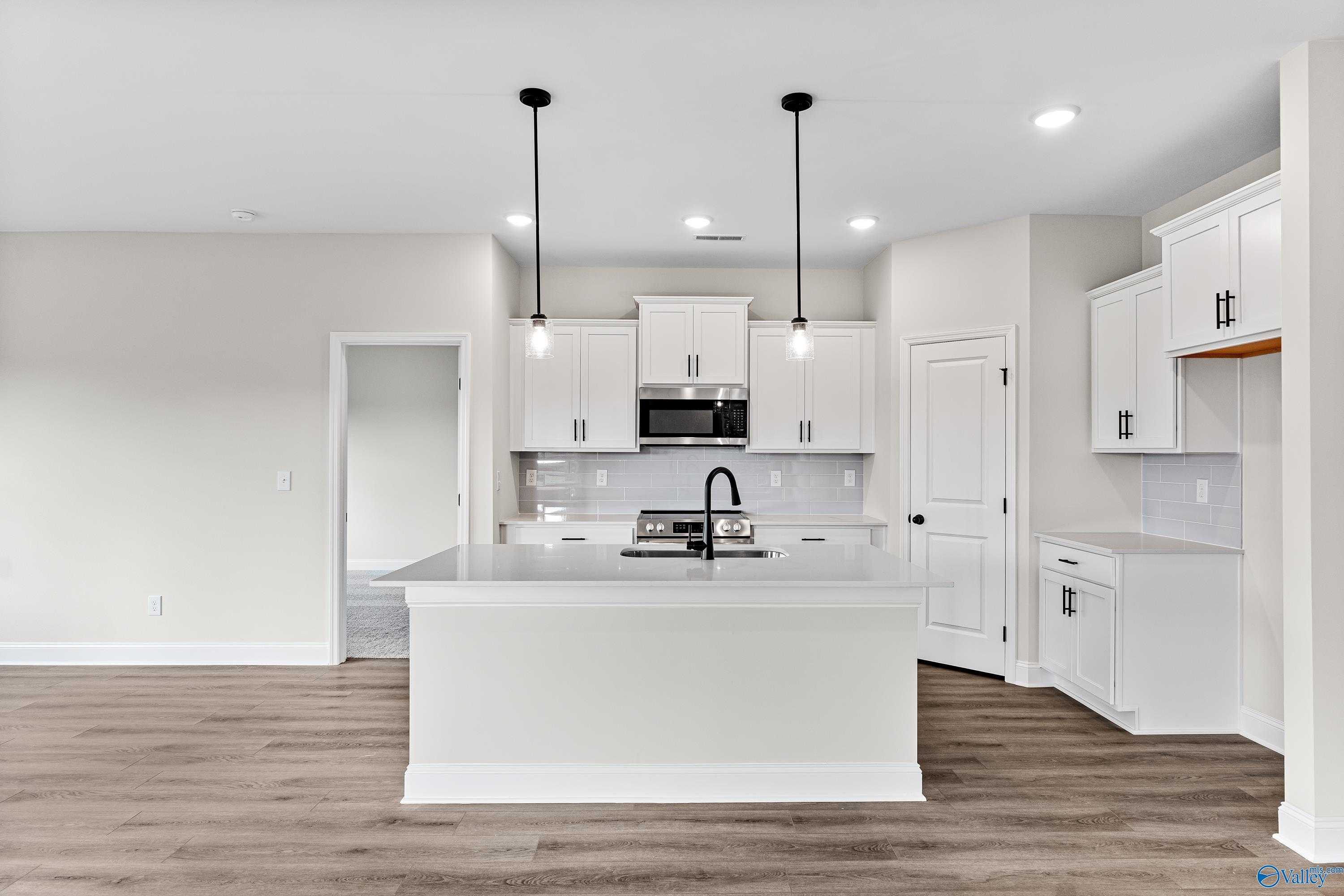 Modern open-concept kitchen with white cabinets, large island, stainless microwave, and pendant lights in Davidson Homes The Franklin B, Hazel Green, Alabama