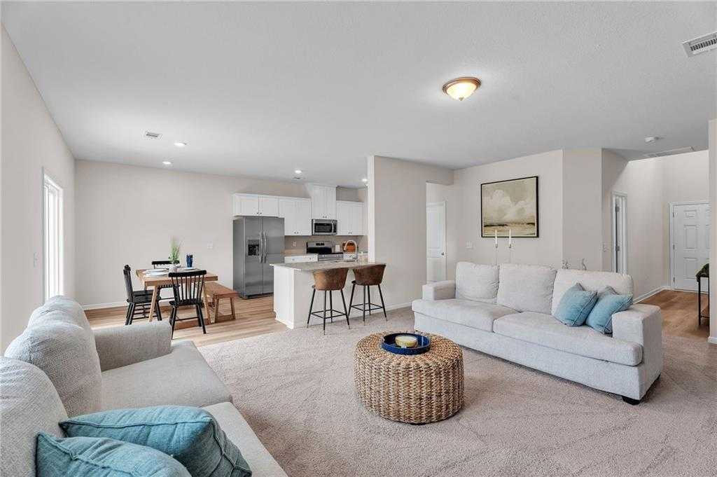 Open-concept living room with white sofas, woven coffee table, dining nook, and stainless kitchen island in Davidson Homes The Bartlett, Phenix City
