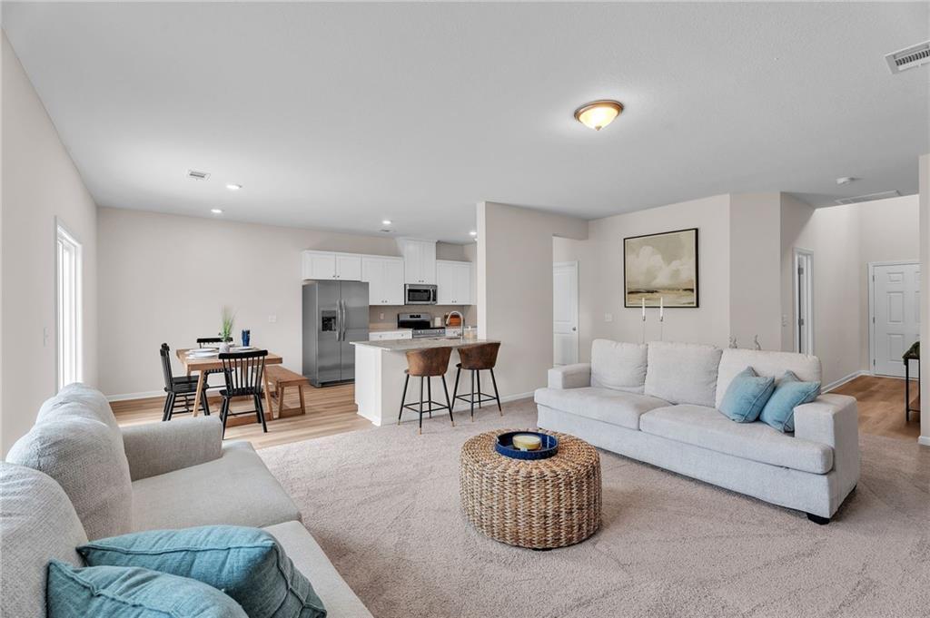 Open-concept living room with white sofas, woven coffee table, dining nook, and stainless kitchen island in Davidson Homes The Bartlett, Phenix City