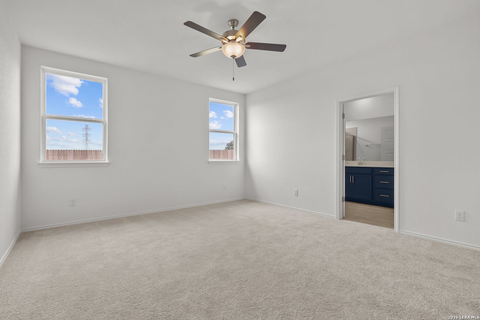 Bright bedroom with ceiling fan, large windows to fenced backyard, adjacent bath with dark cabinets in The Glenwood E, Elmendorf, Texas