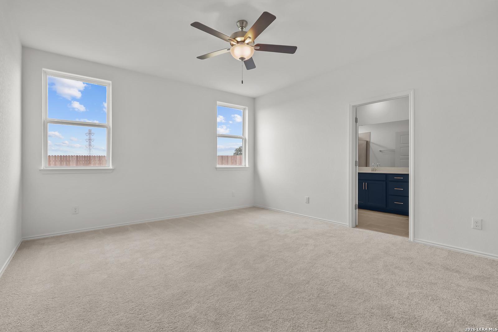 Bright bedroom with ceiling fan, large windows to fenced backyard, adjacent bath with dark cabinets in The Glenwood E, Elmendorf, Texas
