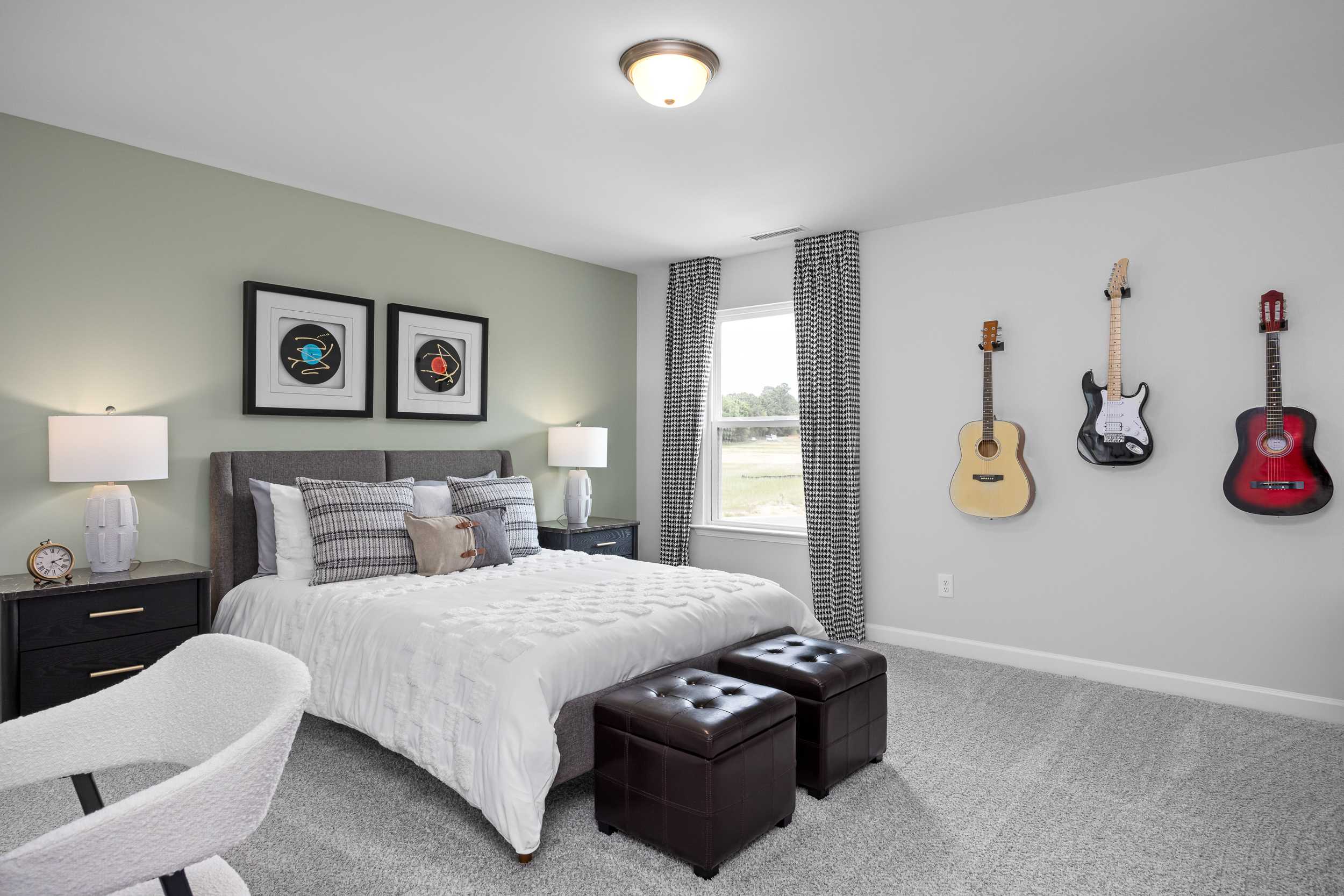 Spacious secondary bedroom in The Magnolia A featuring light green walls, king bed, wall-mounted guitars, and vinyl record art in Mooresville NC home