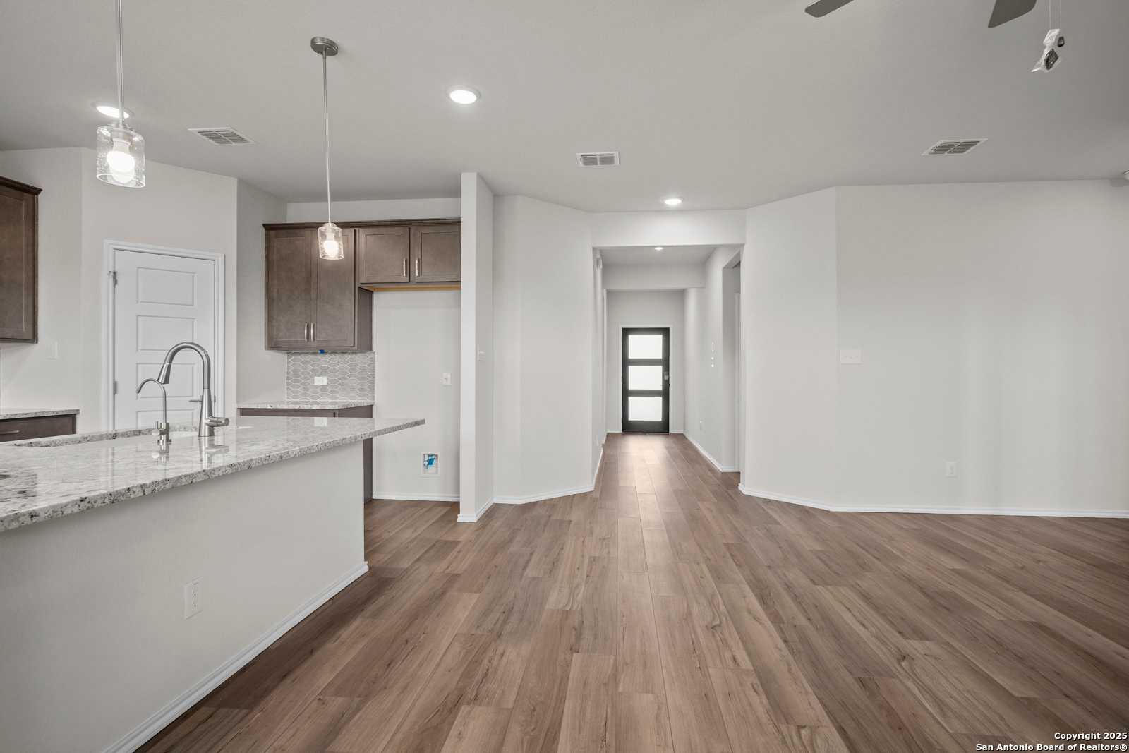 Modern kitchen island with granite countertop, stainless sink, and open hallway in 3-bedroom Davidson Homes The Asheville J, San Antonio