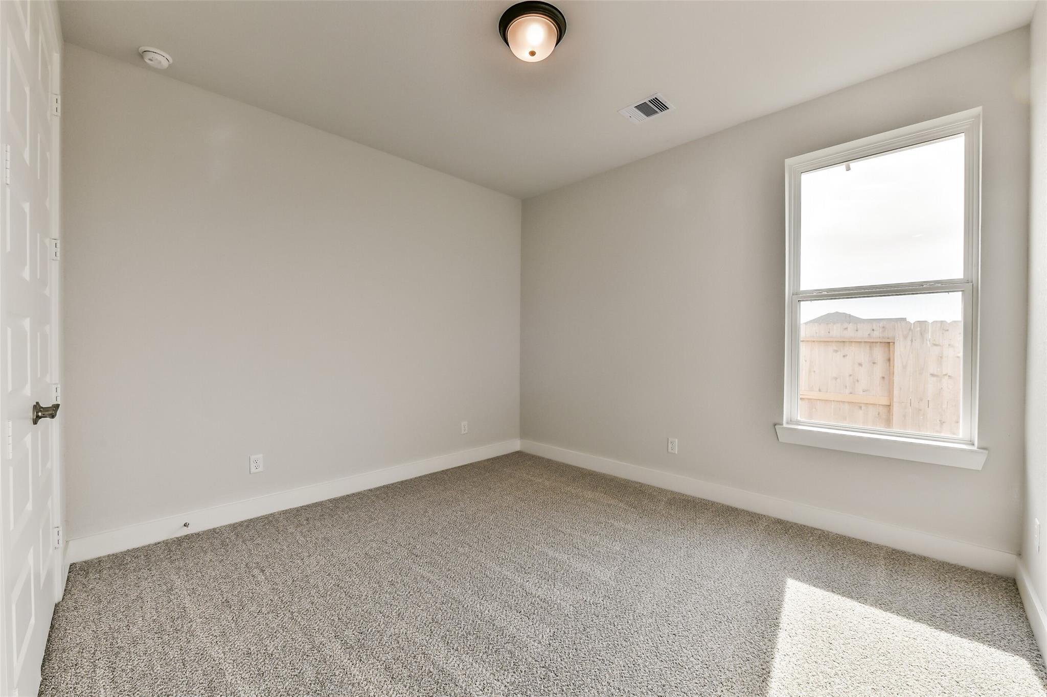 Empty secondary bedroom with neutral walls, carpeted floor, large window, and ceiling light in Davidson Homes The George A, Lago Mar, Texas City