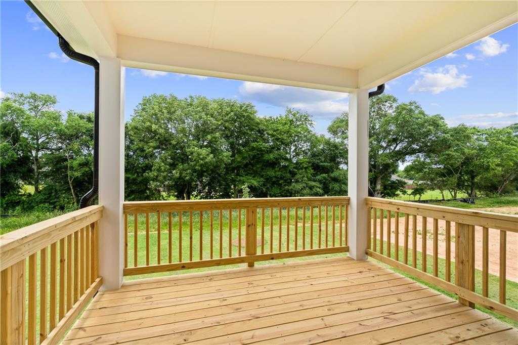 Spacious wooden deck with white-columned porch overlooking lush green backyard and trees in Davidson Homes The Hickory B at Wehunt Meadows, Hoschton, Georgia