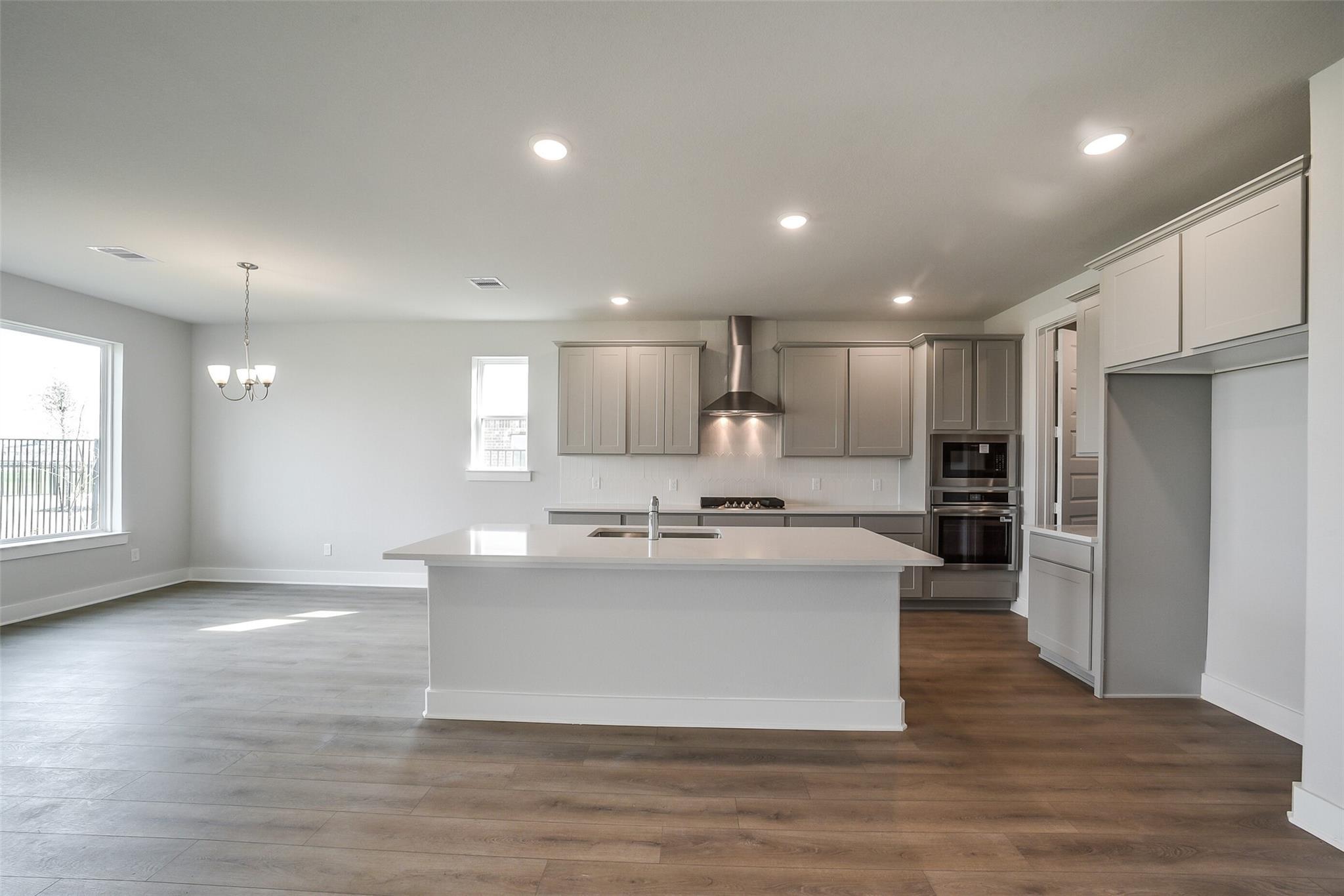 Modern open-concept kitchen with white shaker cabinets, quartz island sink, stainless appliances in Davidson Homes The Philip B, Rosharon, Texas