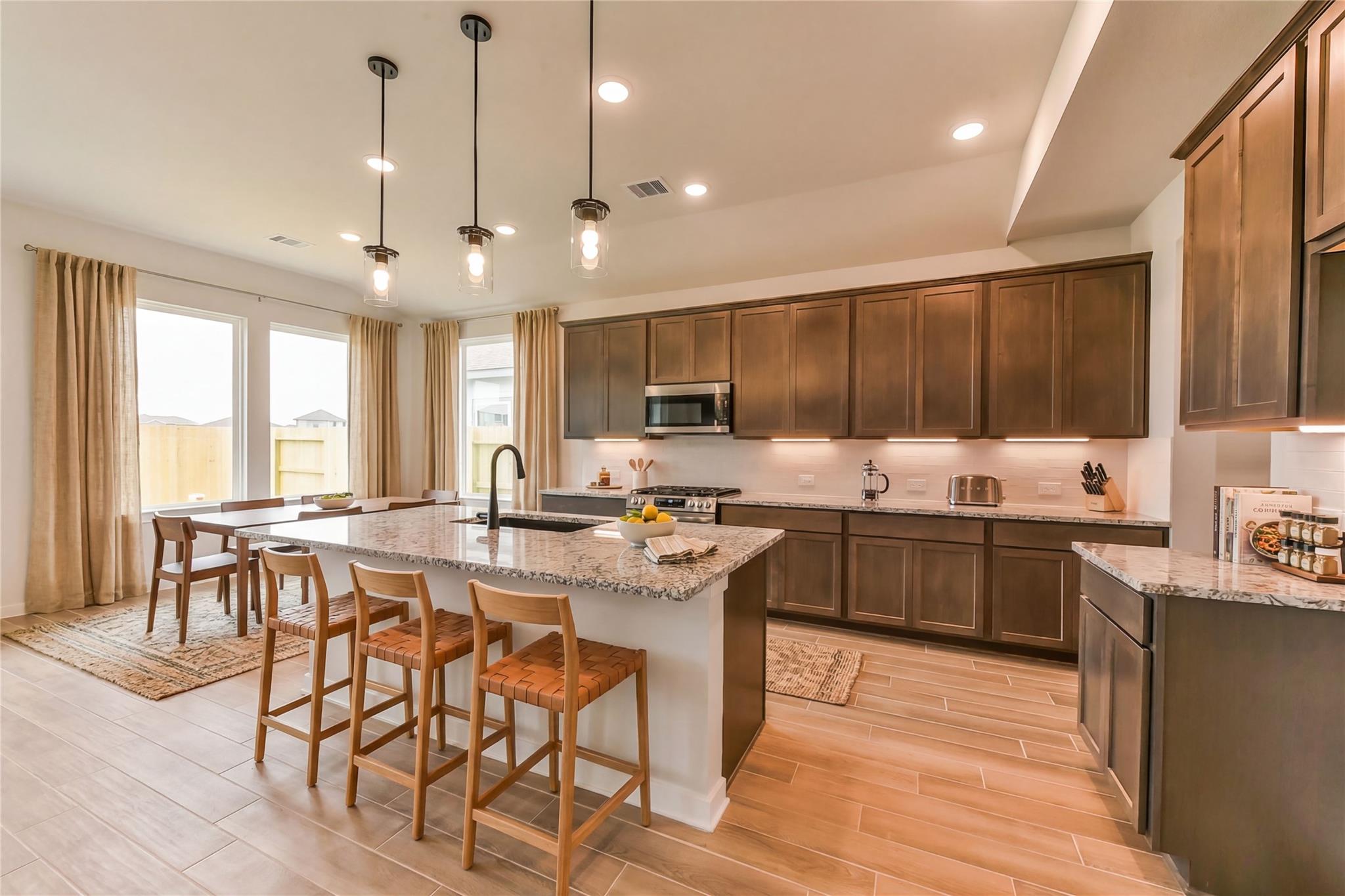 Modern kitchen with granite island, stainless appliances, shaker cabinets, and bar stools in Davidson Homes Sequoia C, Crosby TX
