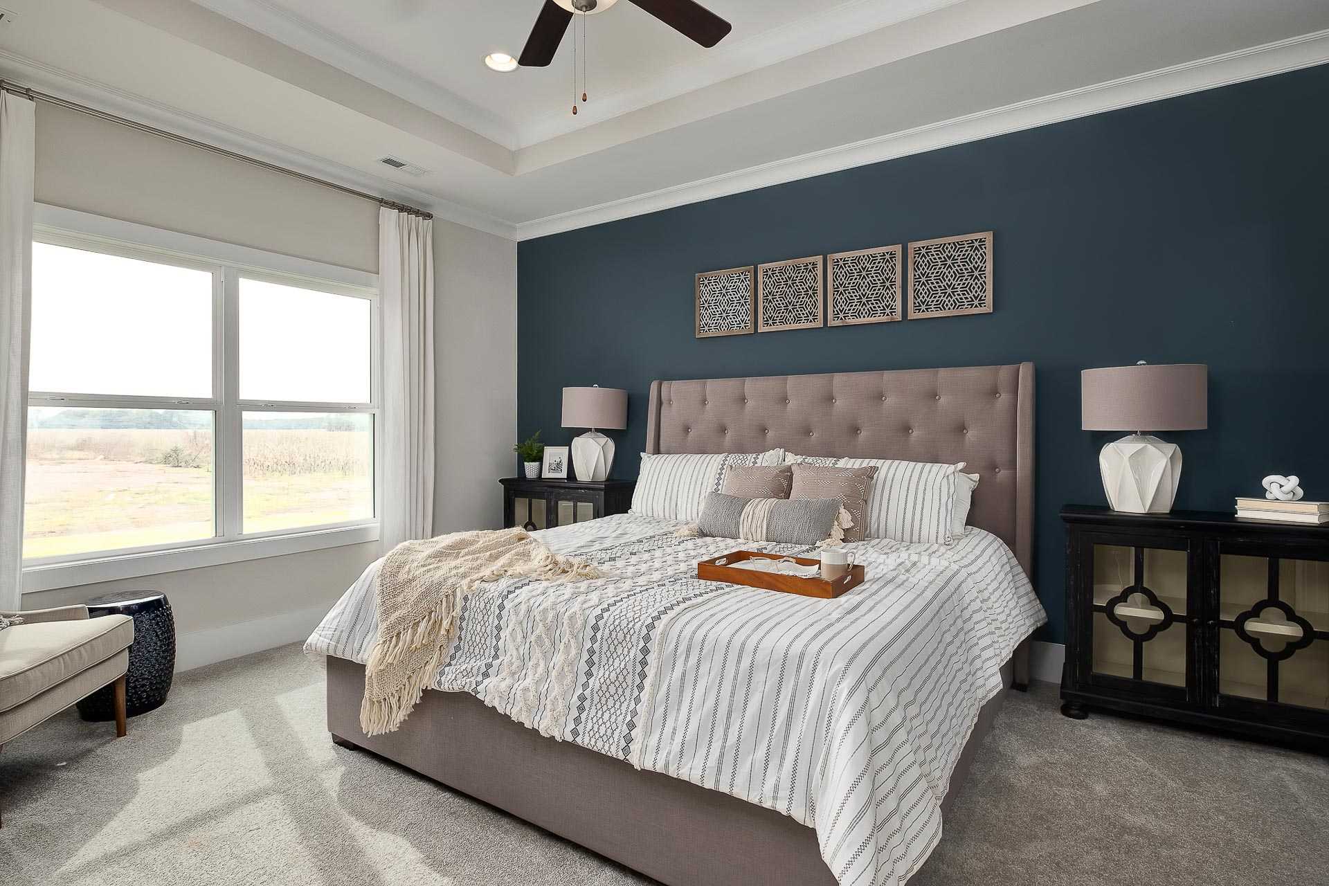Spacious master bedroom in The Everett C featuring navy accent wall, king bed with striped duvet, large windows