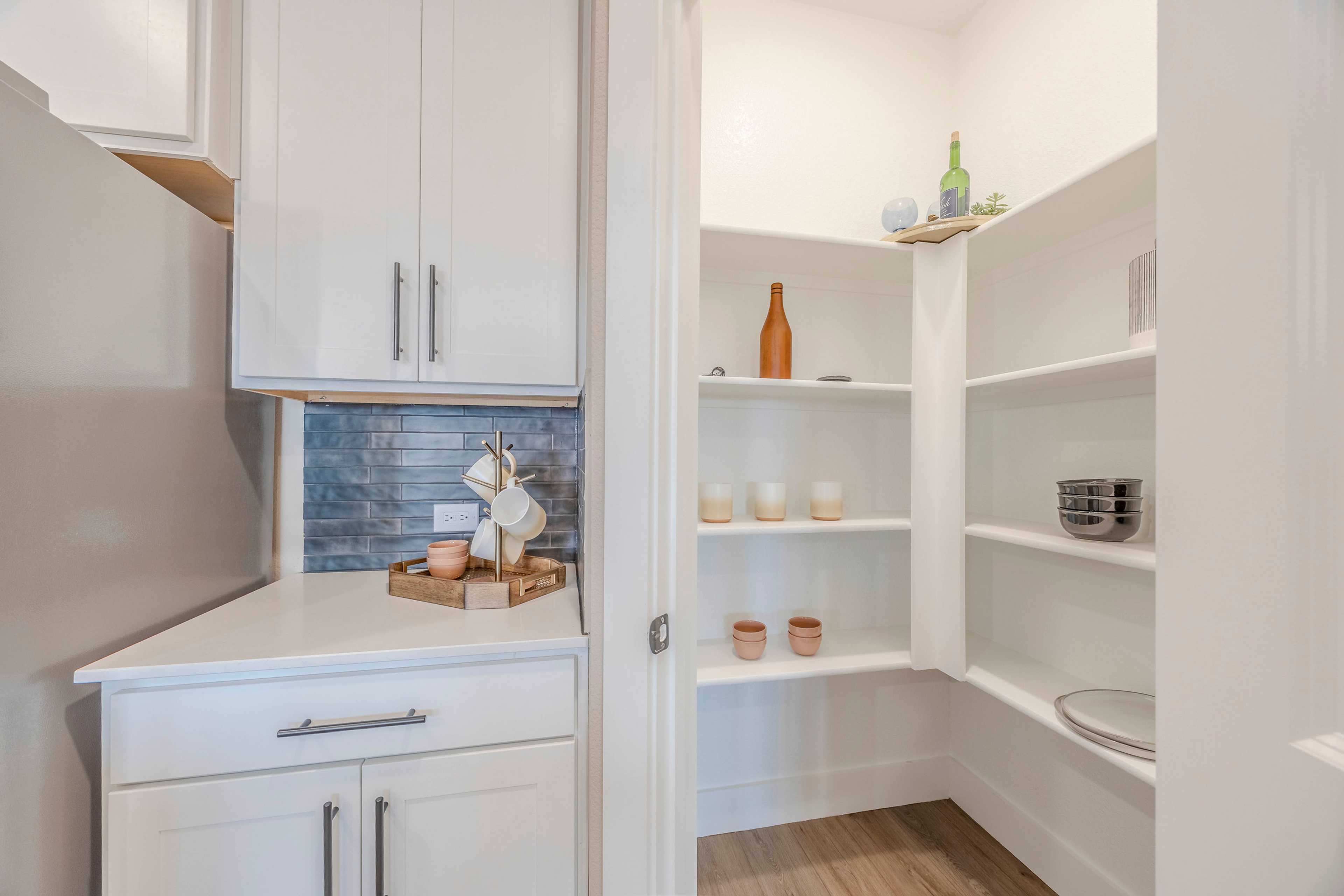 Spacious walk-in pantry in The Rockford home design featuring white shaker cabinets, stocked shelves with dishes, cups and bottles