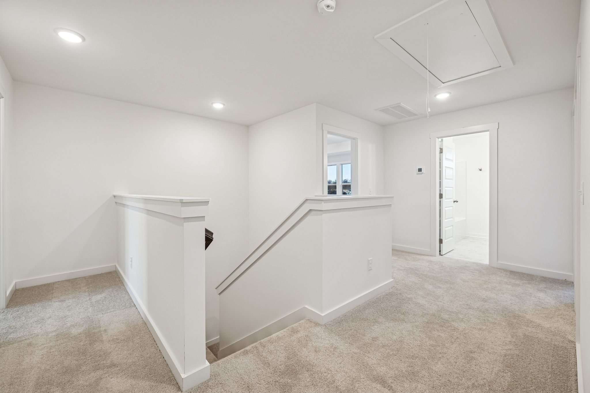 Bright upstairs landing with white-railed staircase, beige carpet, and open bathroom door in The Willow 2-story home, Calista Farms
