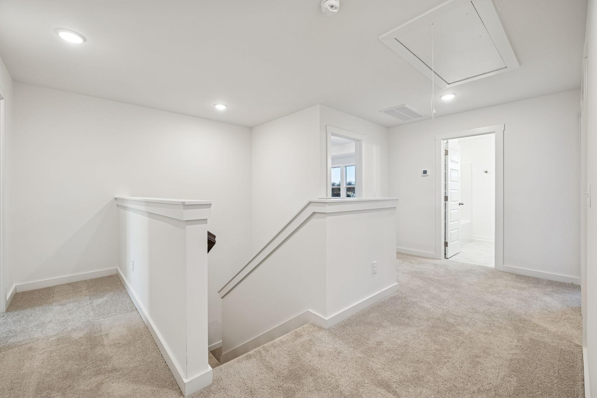 Bright upstairs landing with white-railed staircase, beige carpet, and open bathroom door in The Willow 2-story home, Calista Farms