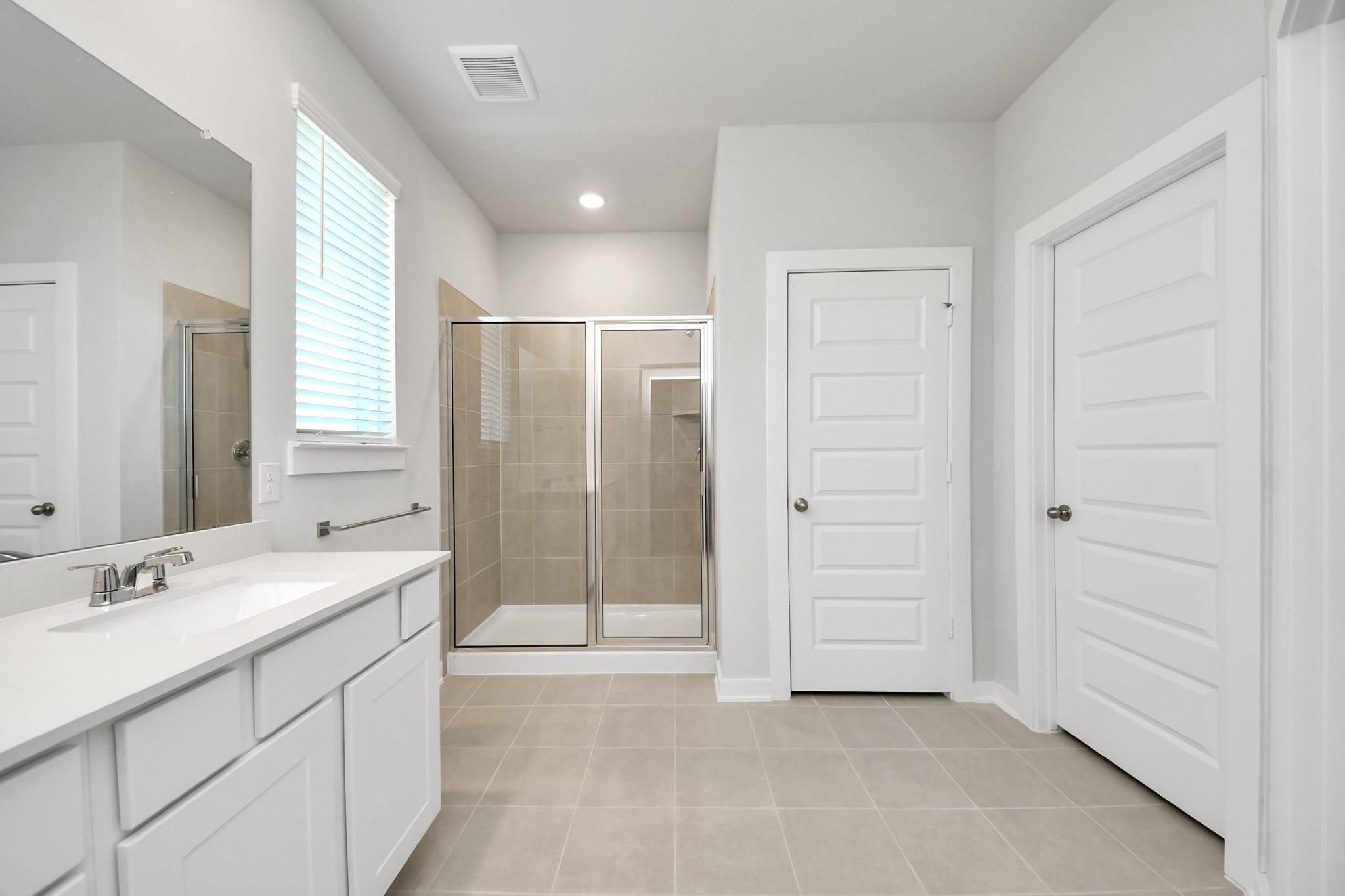 Bright primary bathroom with dual-sink vanity, glass shower, and tile flooring in Davidson Homes The Costa A, Emberly, Beasley Texas