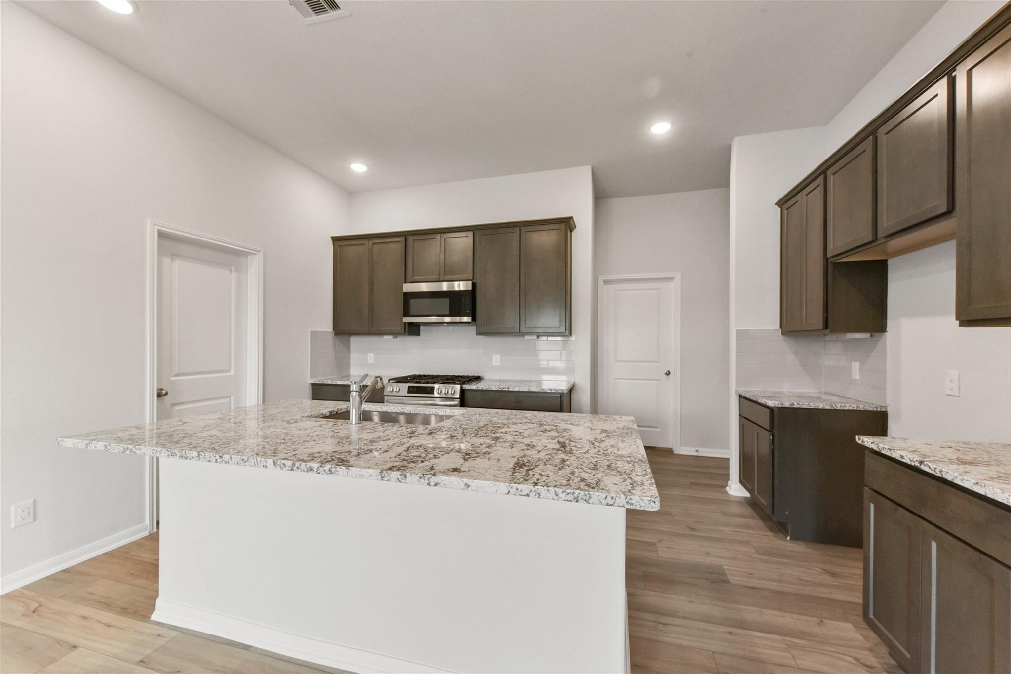 Modern kitchen with brown shaker cabinets, granite island sink, stainless appliances in Davidson Homes The Laguna B, Magnolia, Texas