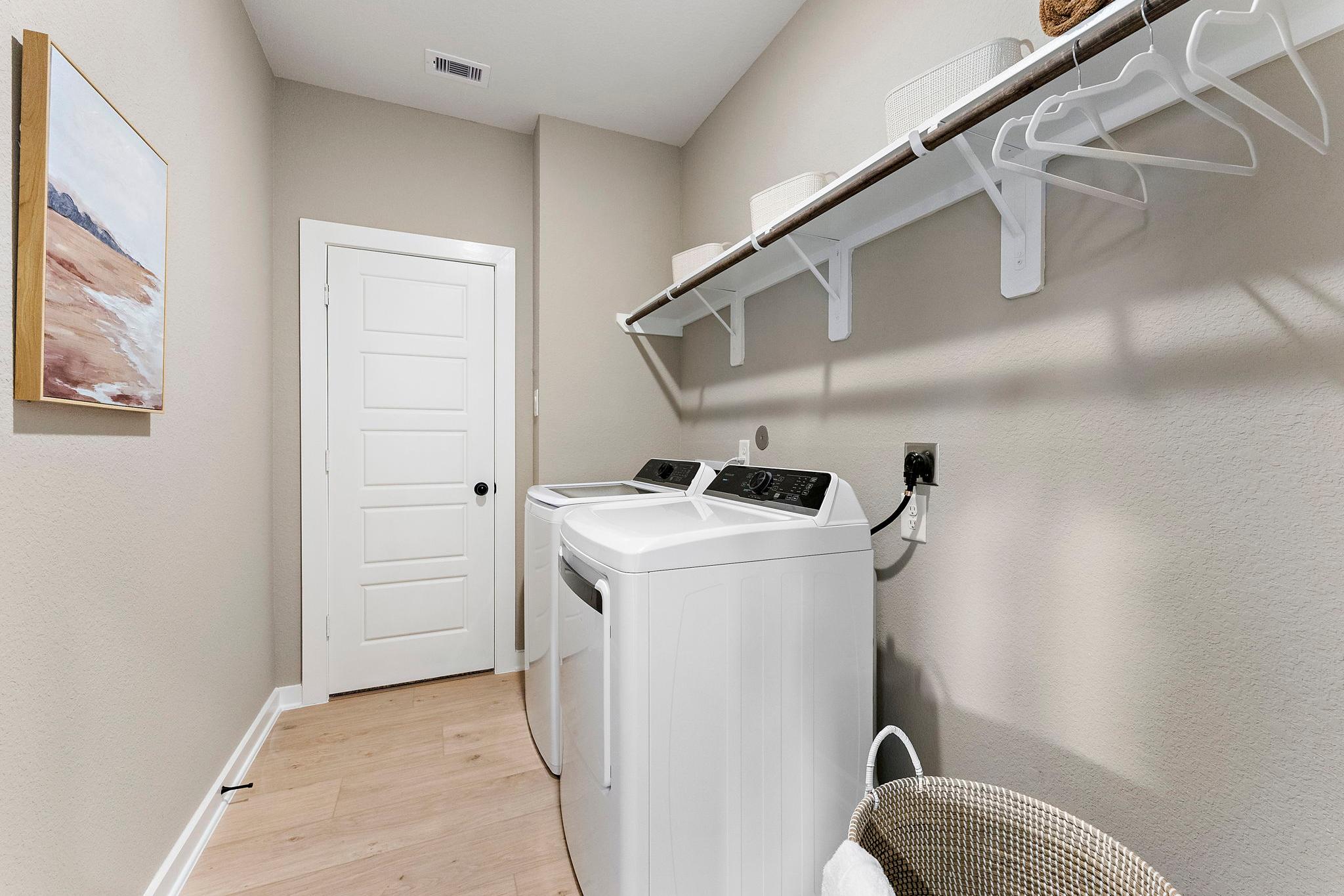 Spacious laundry room in Sundance Cove Crosby Texas with white washer dryer wooden shelves and beach art