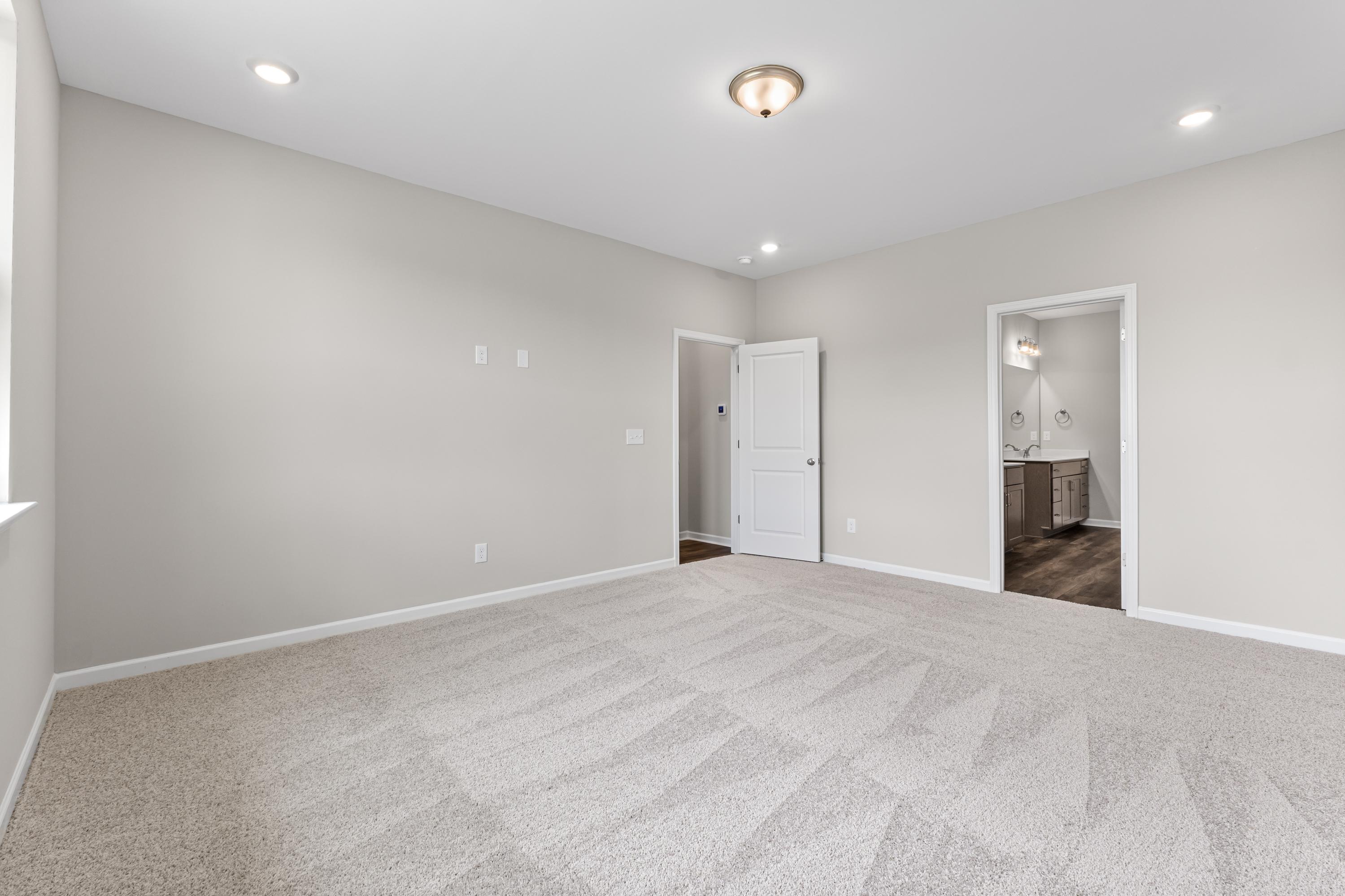 Spacious master bedroom in The Haven E with light gray walls, beige carpet, adjacent bath vanity, and recessed lighting