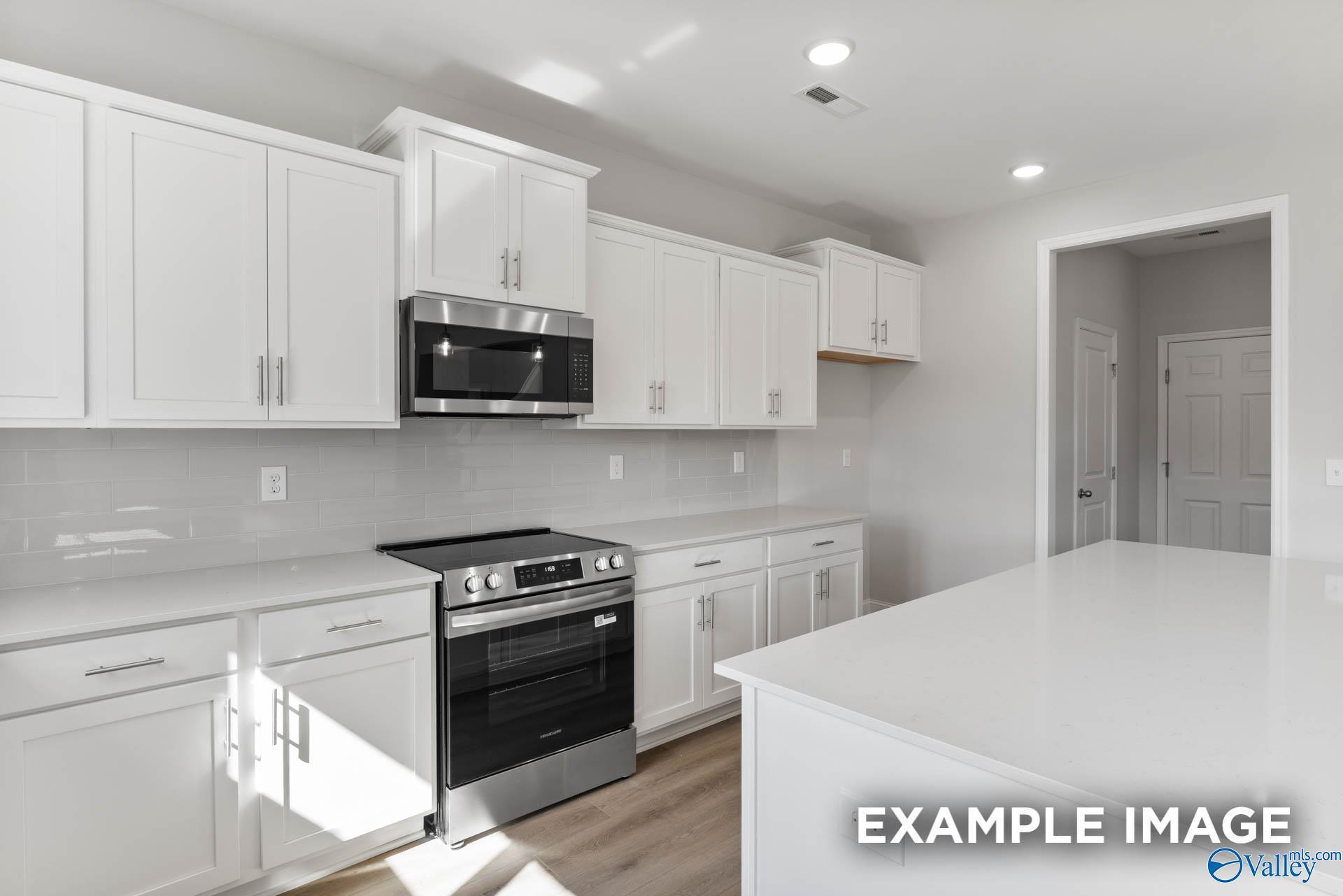 Modern white shaker kitchen with stainless steel appliances, subway tile backsplash, and quartz island in Davidson Homes Chelsea D, New Market, Alabama