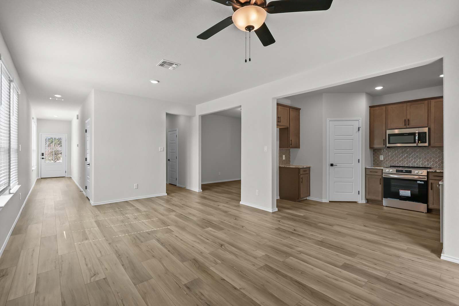 Open-concept kitchen and living area in The Florence B featuring modern wood-look flooring and stainless steel appliances.