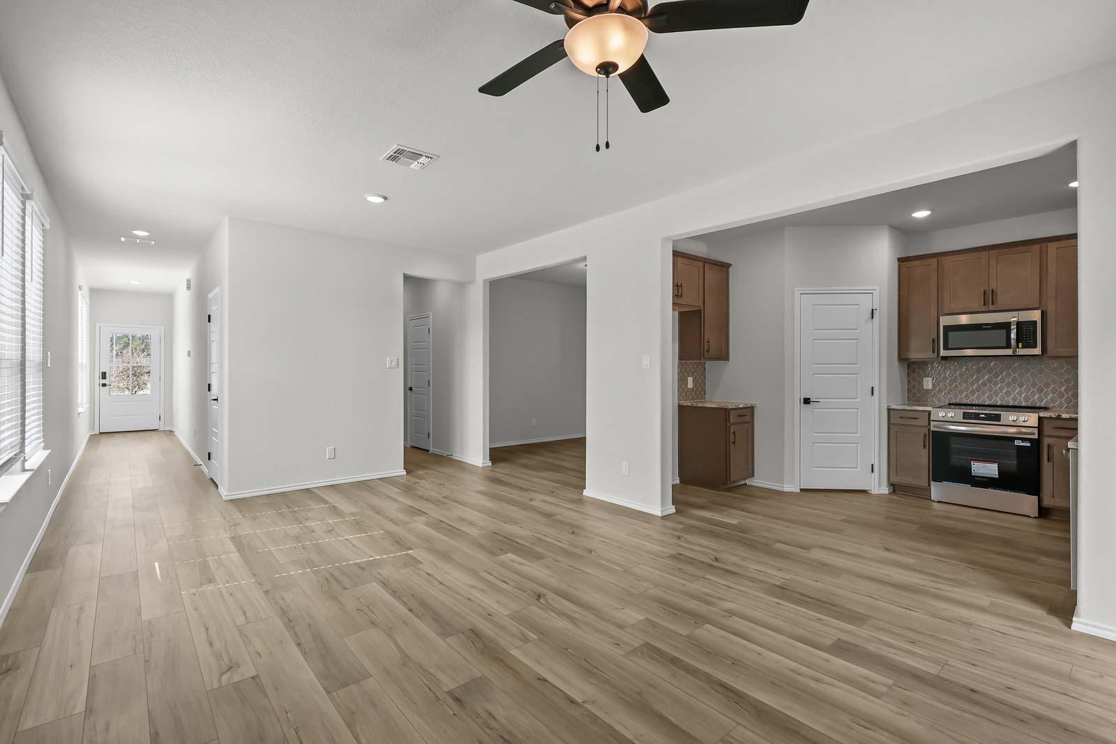 Open-concept kitchen and living area in The Florence B featuring modern wood-look flooring and stainless steel appliances.