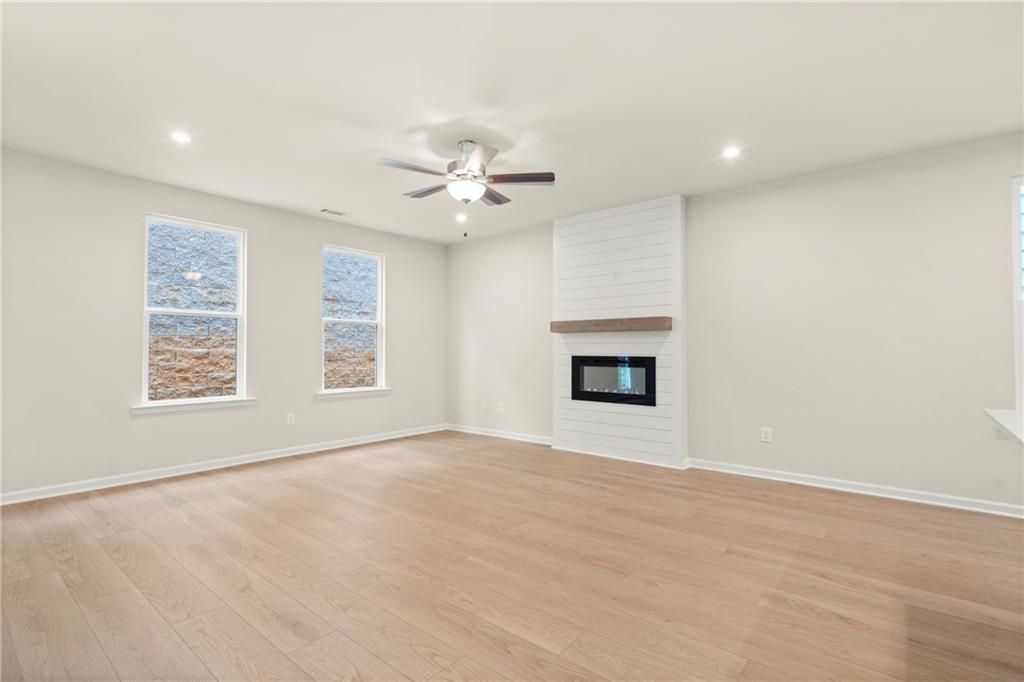 Cozy living room featuring modern white fireplace, ceiling fan, large windows, and hardwood floors in Davidson Homes The Cary A, Kennesaw, Georgia