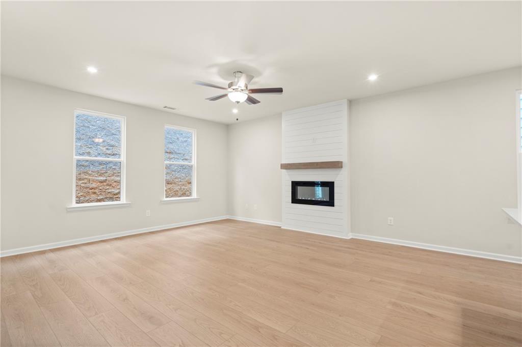 Cozy living room featuring modern white fireplace, ceiling fan, large windows, and hardwood floors in Davidson Homes The Cary A, Kennesaw, Georgia