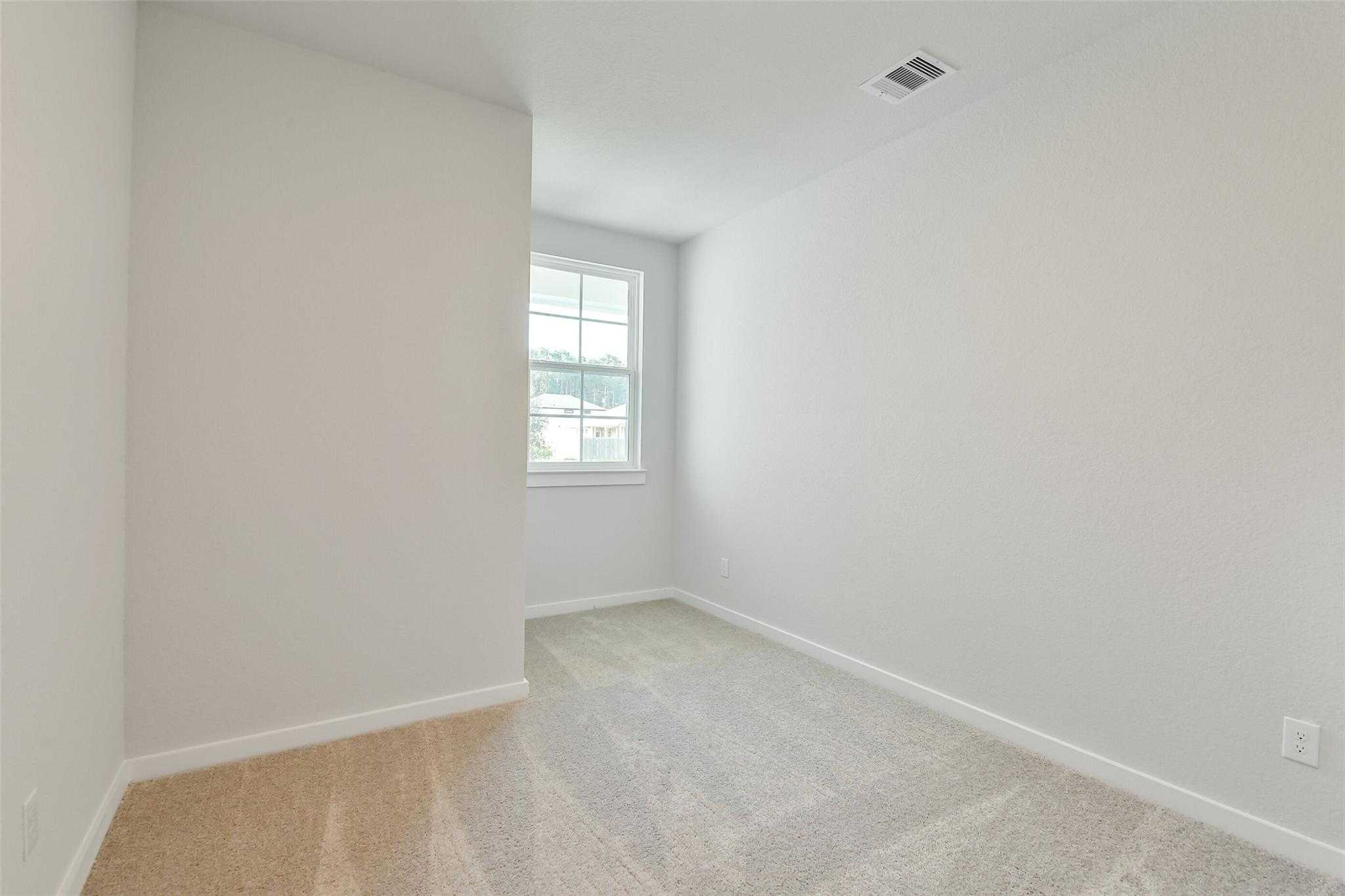 Bright secondary bedroom with beige carpet, white walls, and large window in Davidson Homes The Colorado F, Cleveland, Texas